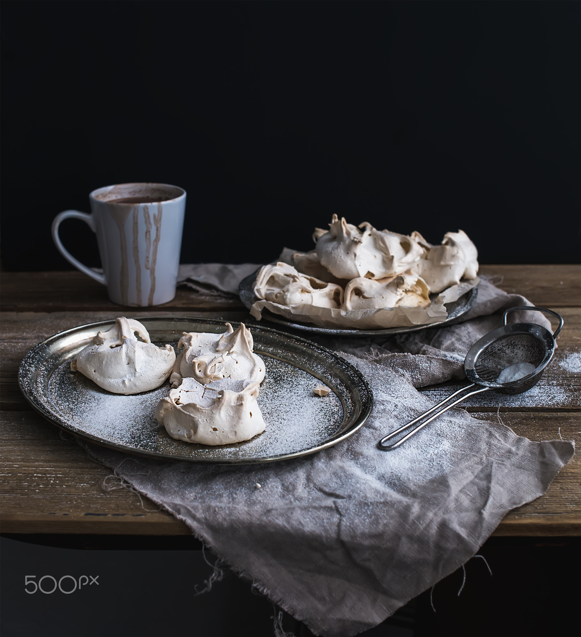 White meringue and mug of hot chocolate on a rustic wooden table. Black backdro