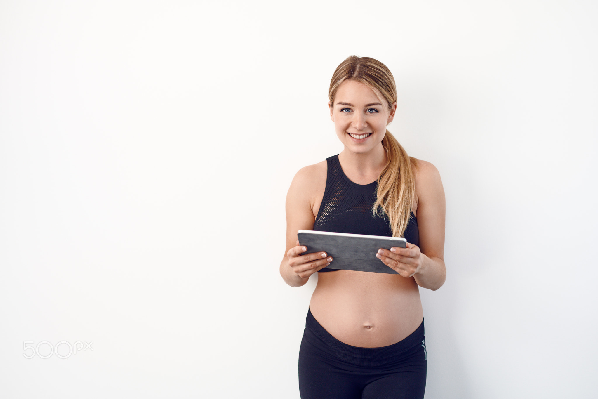 Happy young pregnant woman reading on a tablet pc