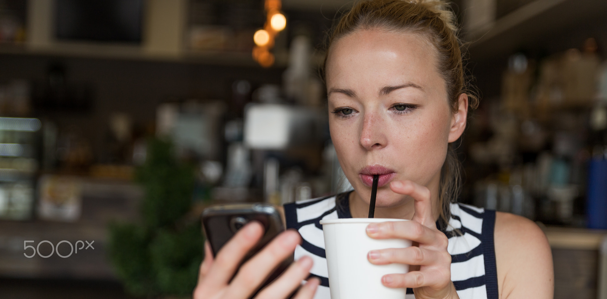 Thoughtful woman reading news on mobile phone while sipping coffee
