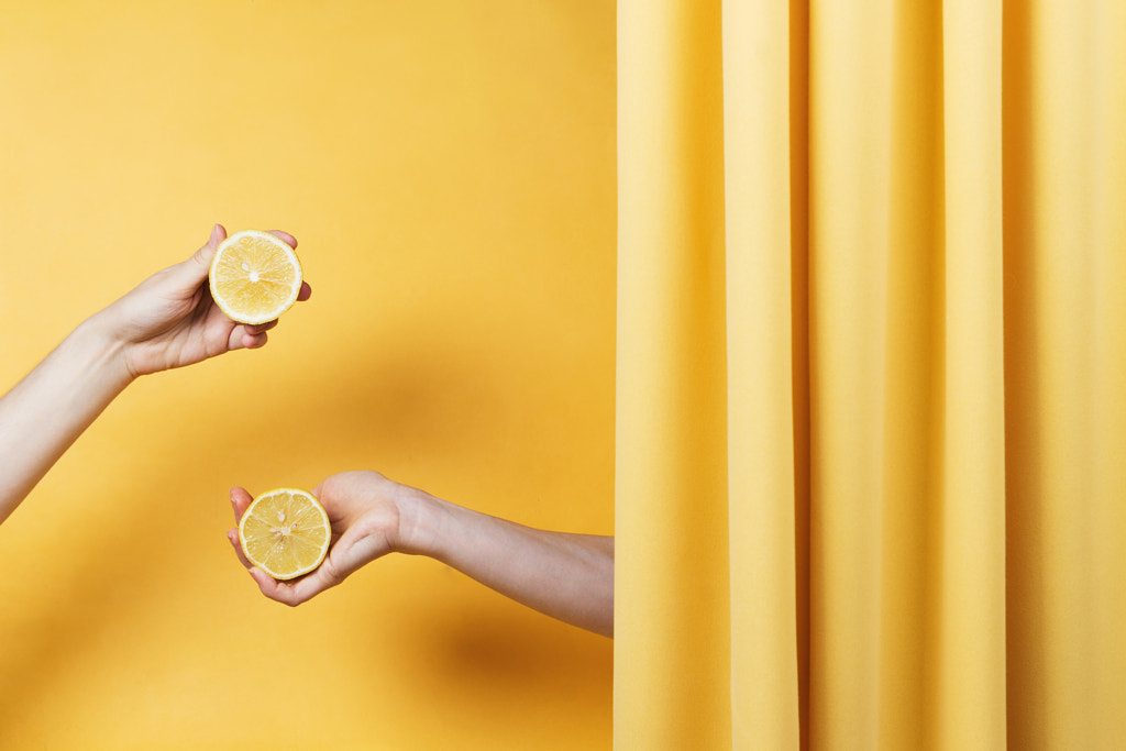 Two women's hands holding cut lemons on yellow, selective focus by Nataly Lavrenkova on 500px.com