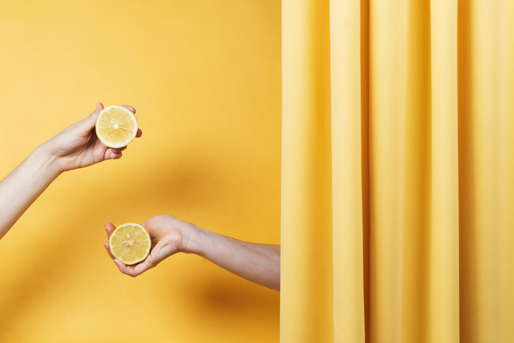 Two women's hands holding cut lemons on yellow, selective focus by Nataly Lavrenkova on 500px.com
