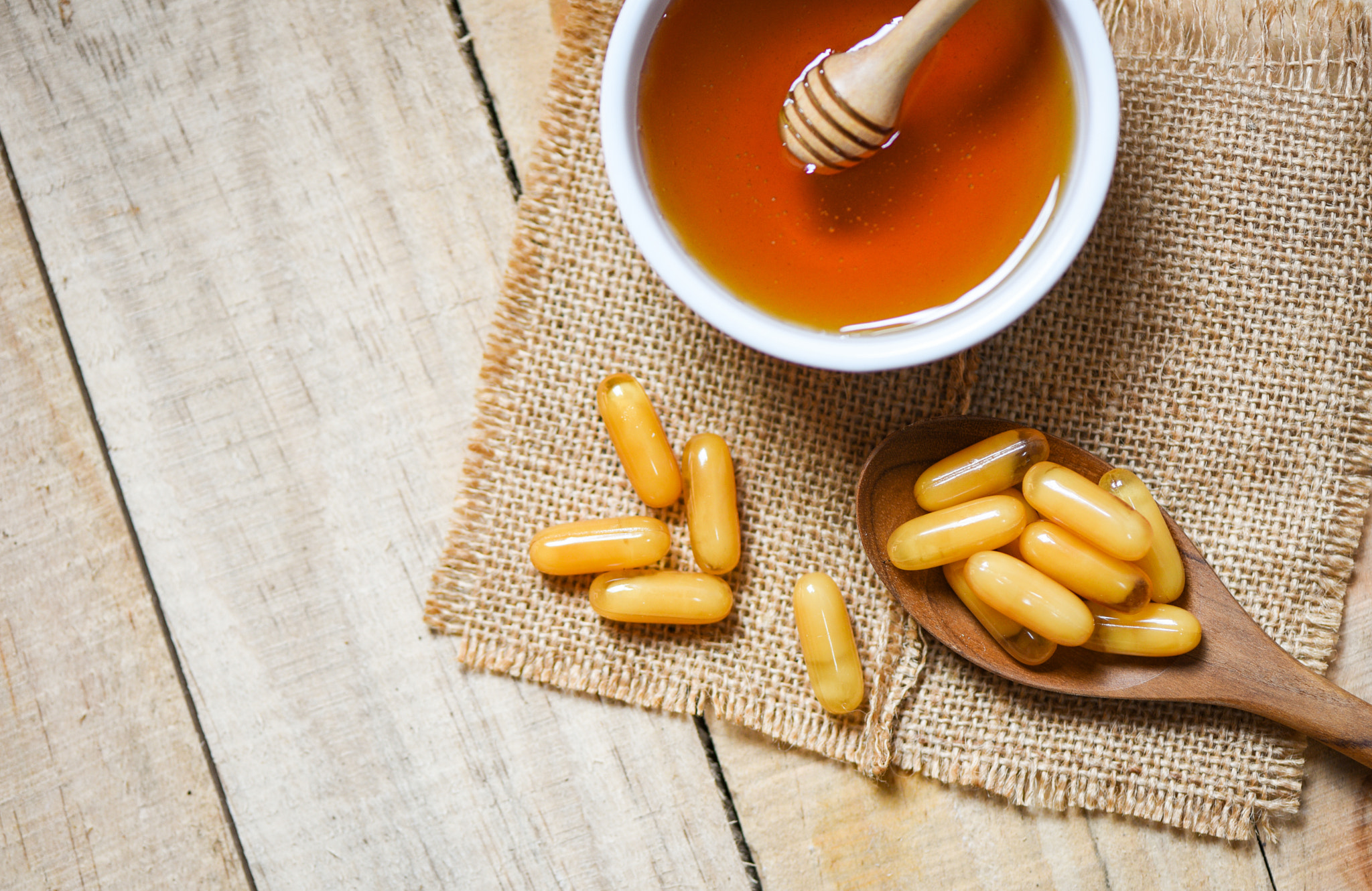 Royal jelly capsules in wooden spoon on sack background and hone