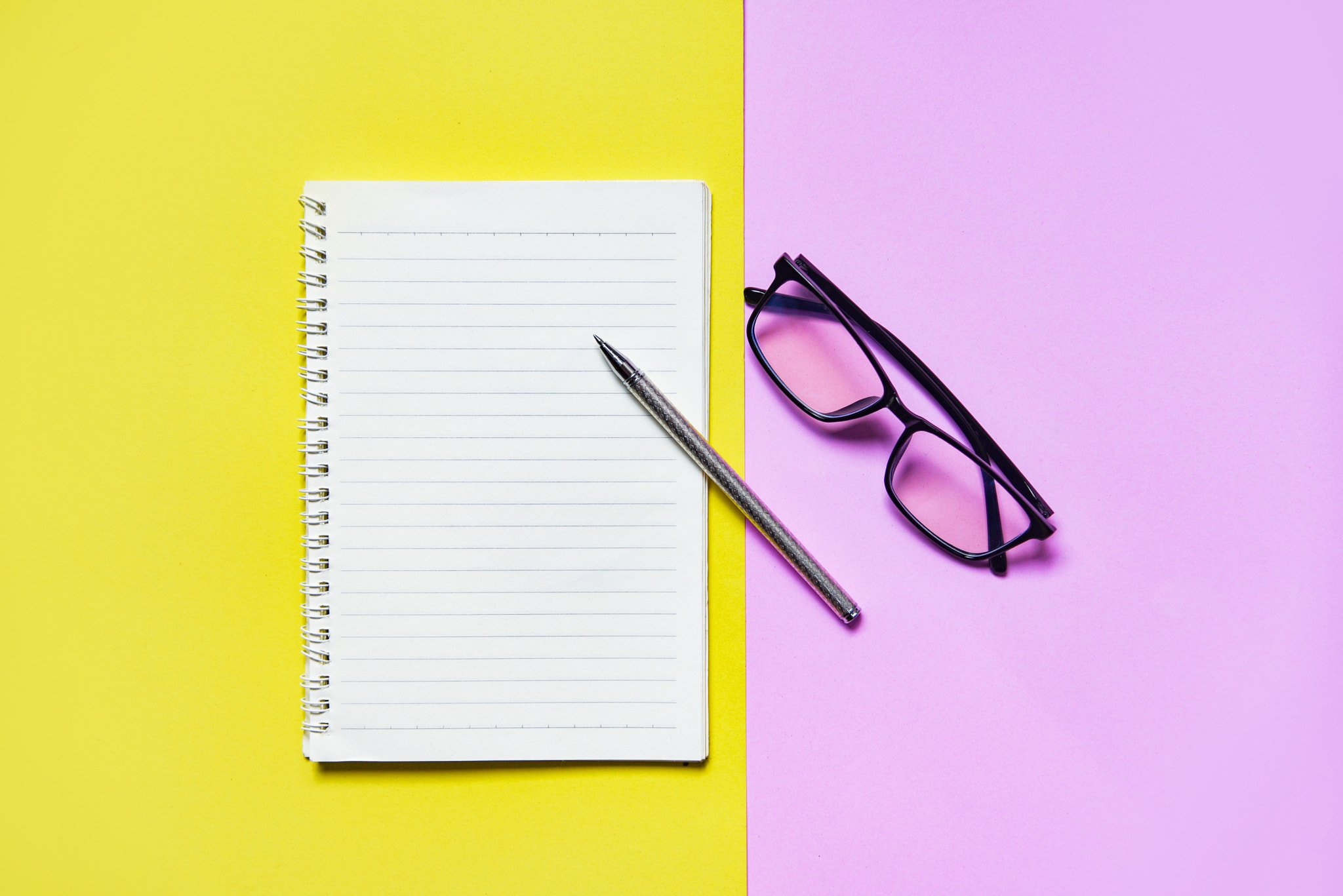 Notepad or notebook paper with pen and glasses on yellow pink fo