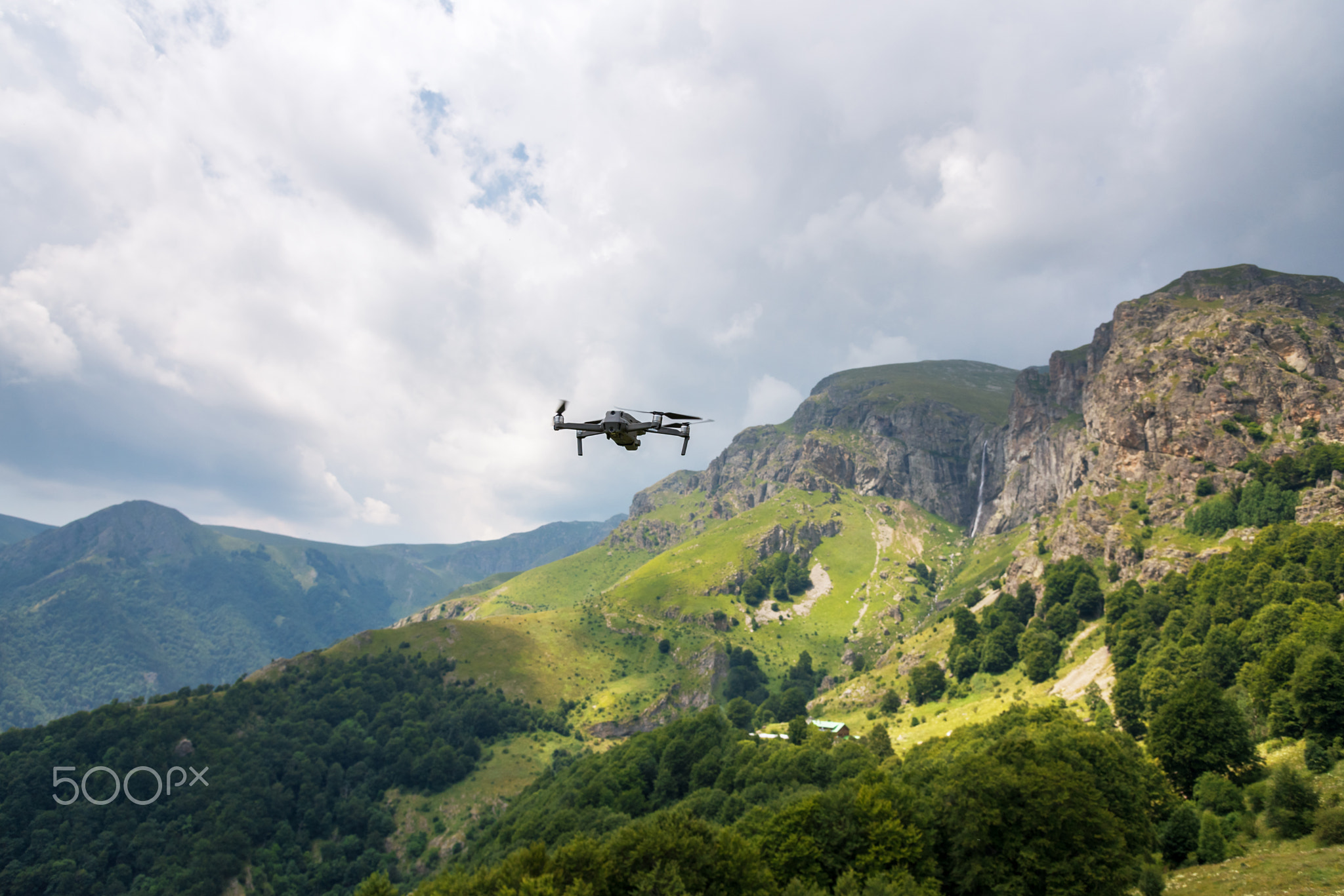 Drone with camera flying over mountain fields.