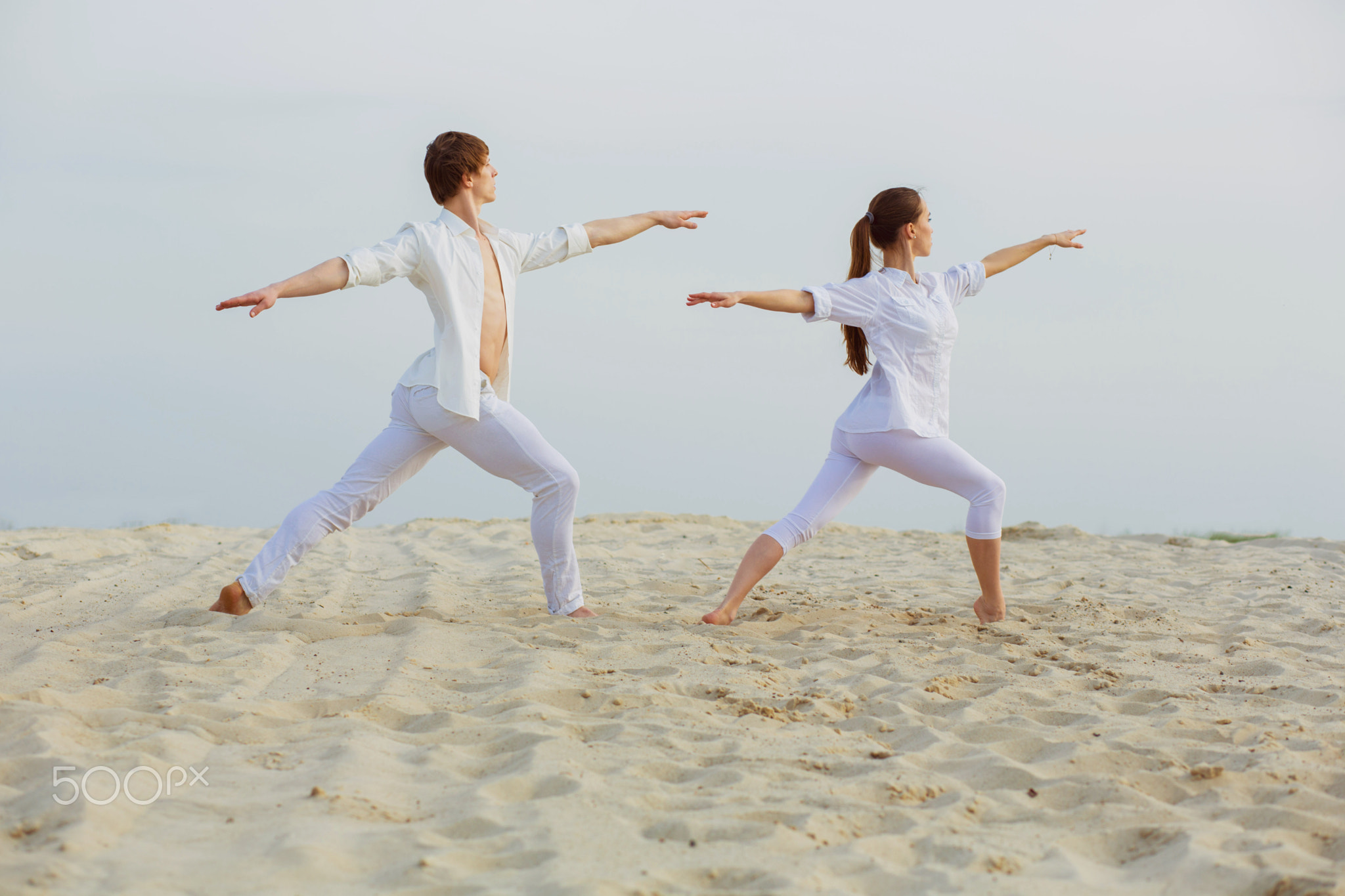 beautiful, athletic couple in white clothes making yoga exercis