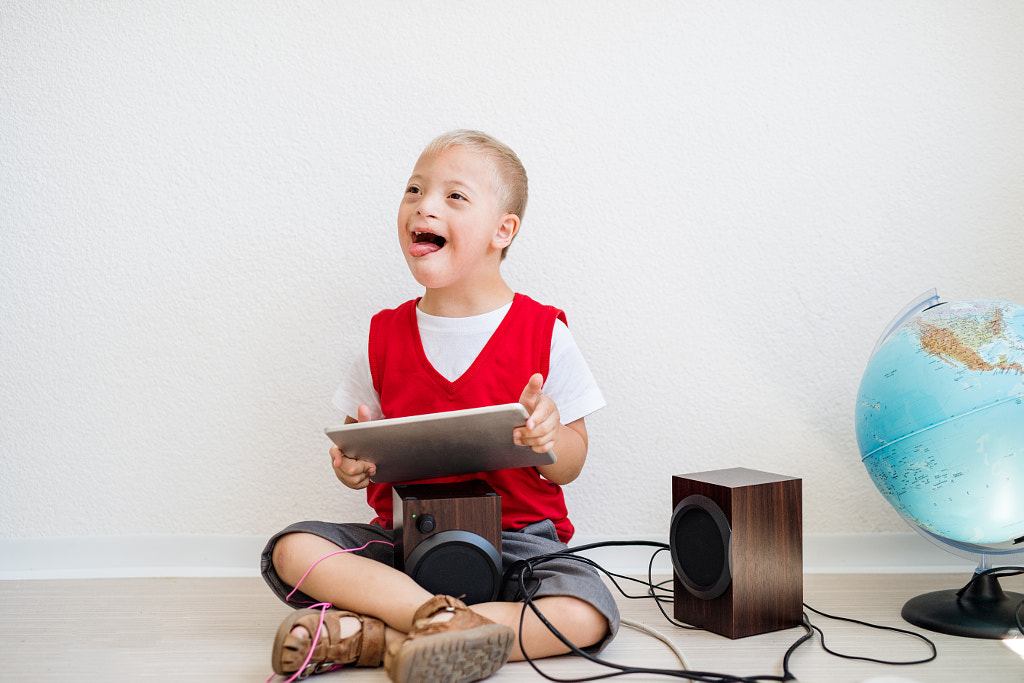 A portrait of down-syndrome school boy with tablet sitting on the floor. by Jozef Polc on 500px.com