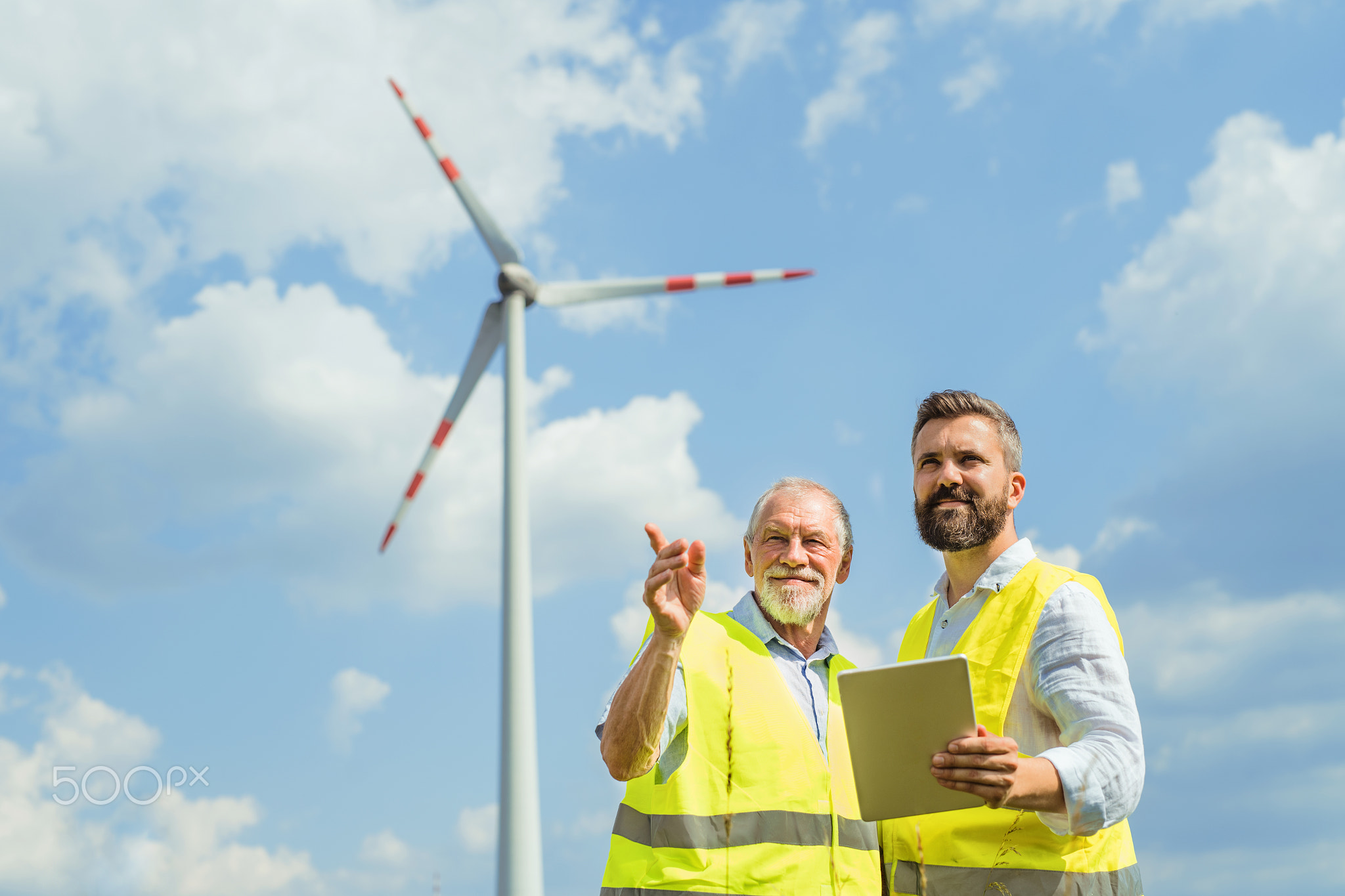 Engineers standing on wind farm, making notes.