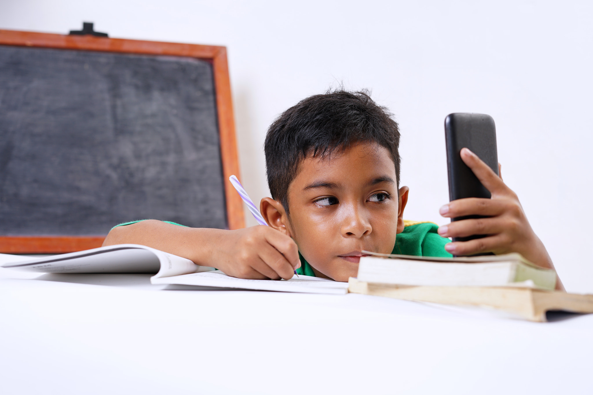 Boy playing with smartphone while doing homework