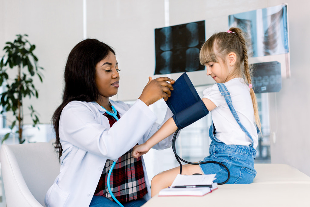 Little girl visiting young female African doctor in hospital. Measuring blood pressure and checking by Sofiia Shunkina on 500px.com