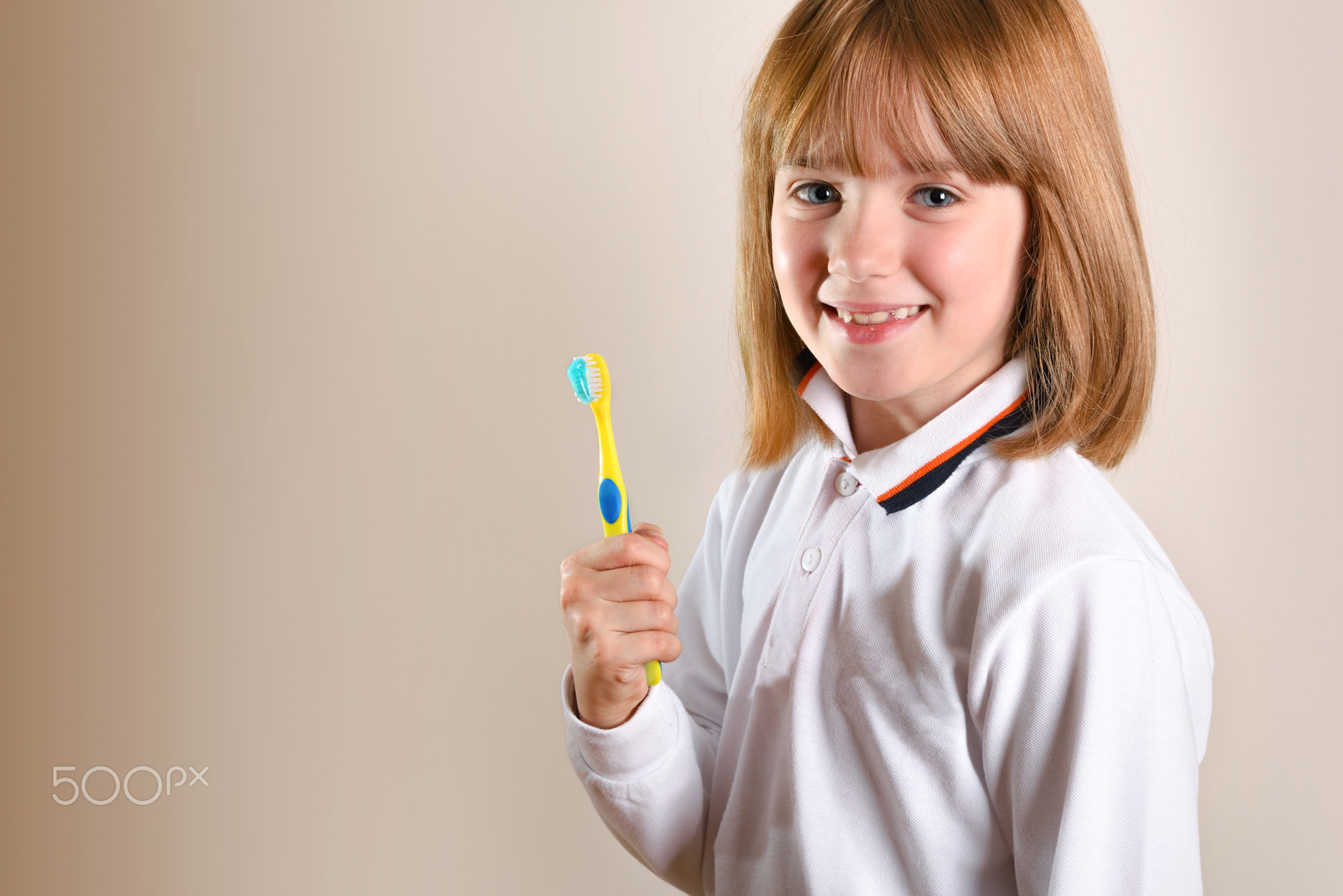 Girl on side showing tooth brush on isolated brown