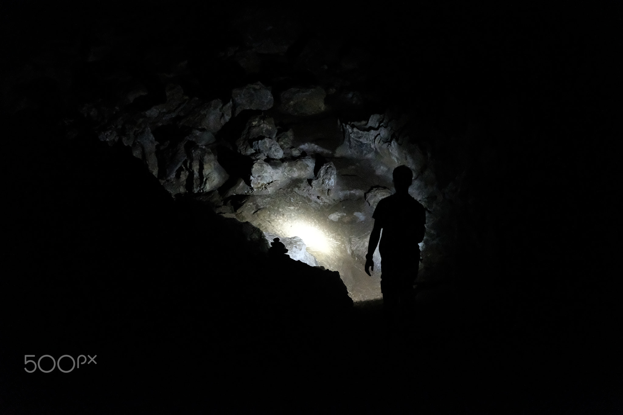 Silhouette of a man exploring a cave with a torch