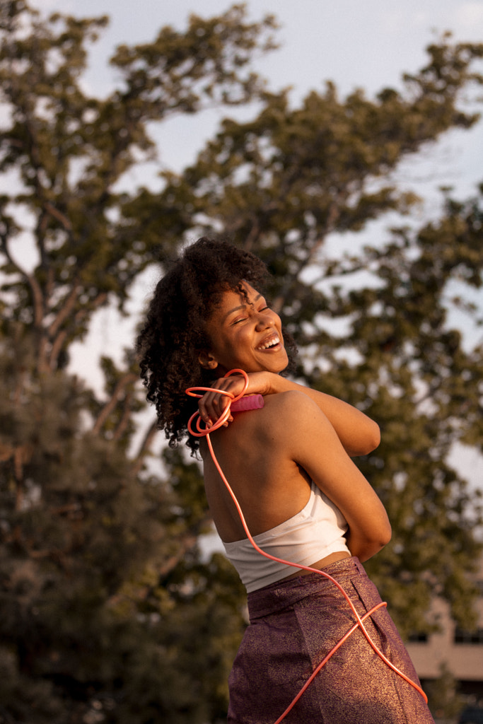 Young African American girl laughing outdoors with arms and rope around body by Hagar Wirba on 500px.com