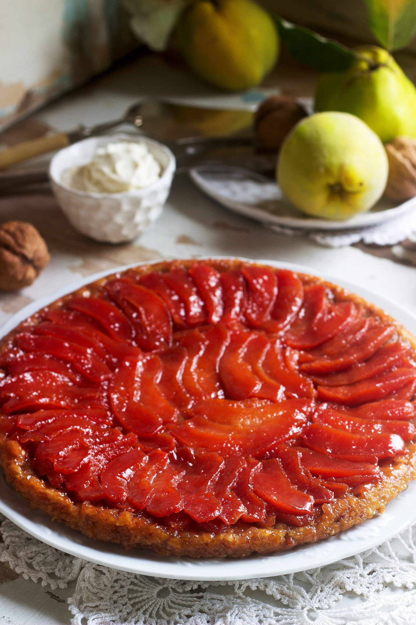 Quince tarte tatin served with whipped cream, quince fruits and walnuts on a wooden surface. Rustic