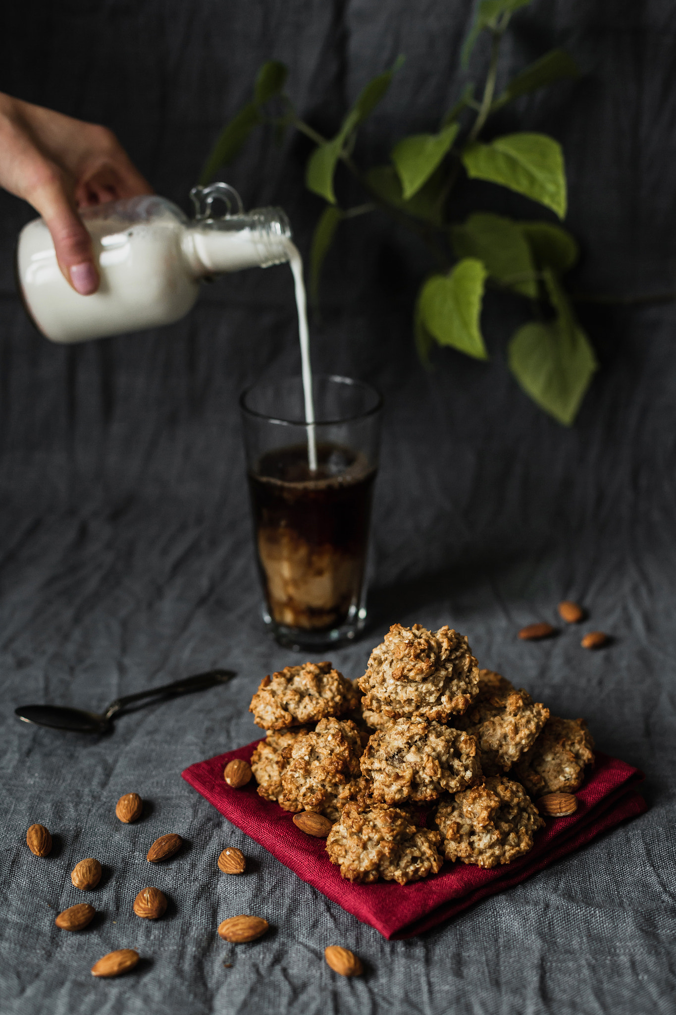 Delicious banana cookies with almond on a red napkin, black coffee in a glass and a hand pouring mil