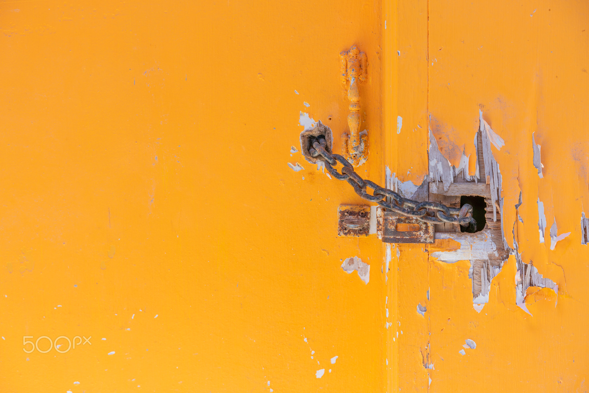 Rusty metal key with chain tie and lock on yellow wooden door