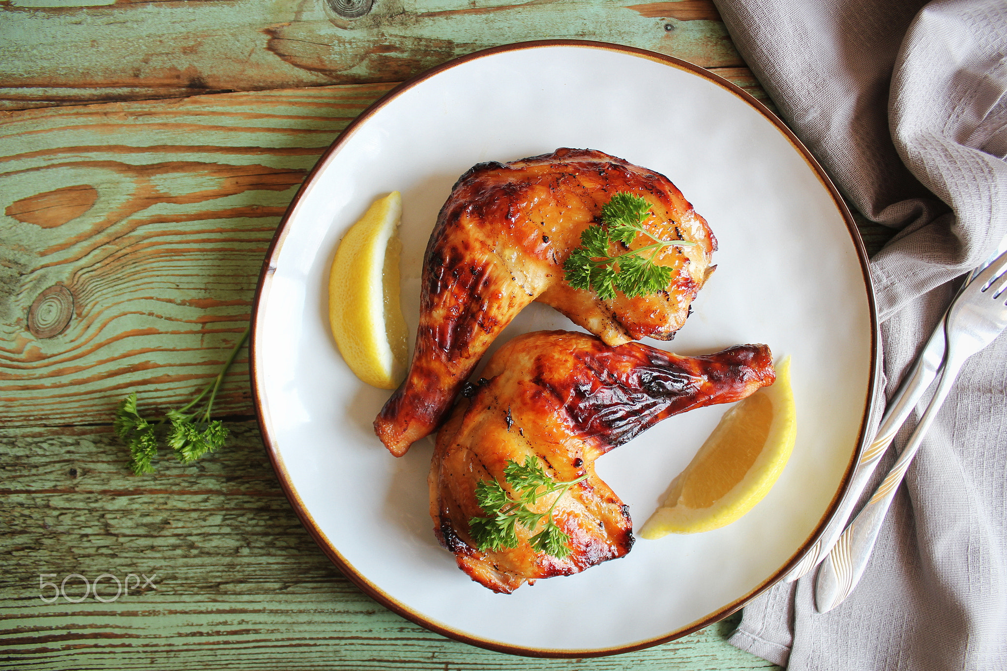 Grilled chicken leg quarters with crispy golden brown skin, lemon, parsley on white plate on dark wo