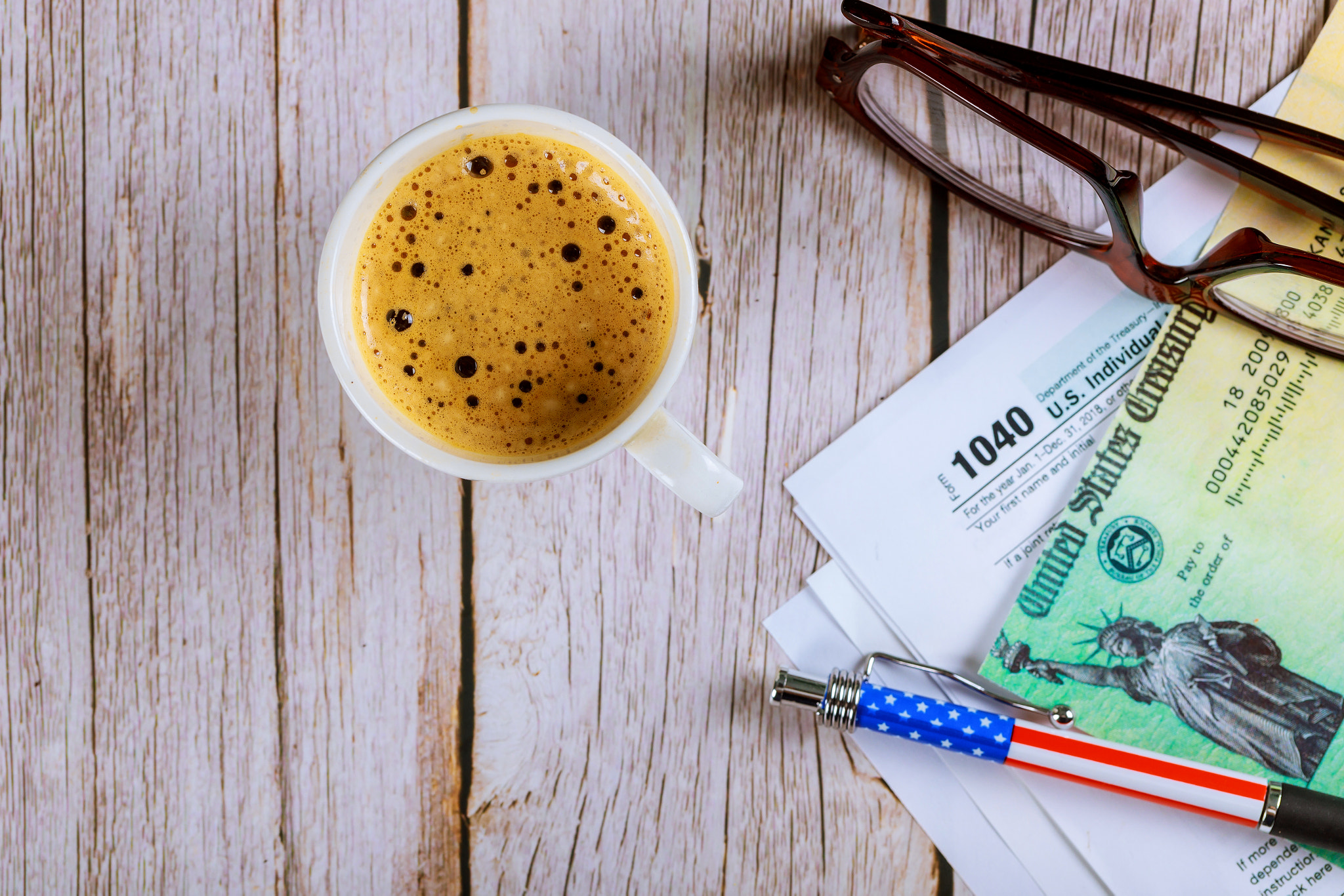 1040 tax forms top view with coffee cup and refund check, pencil with glasses