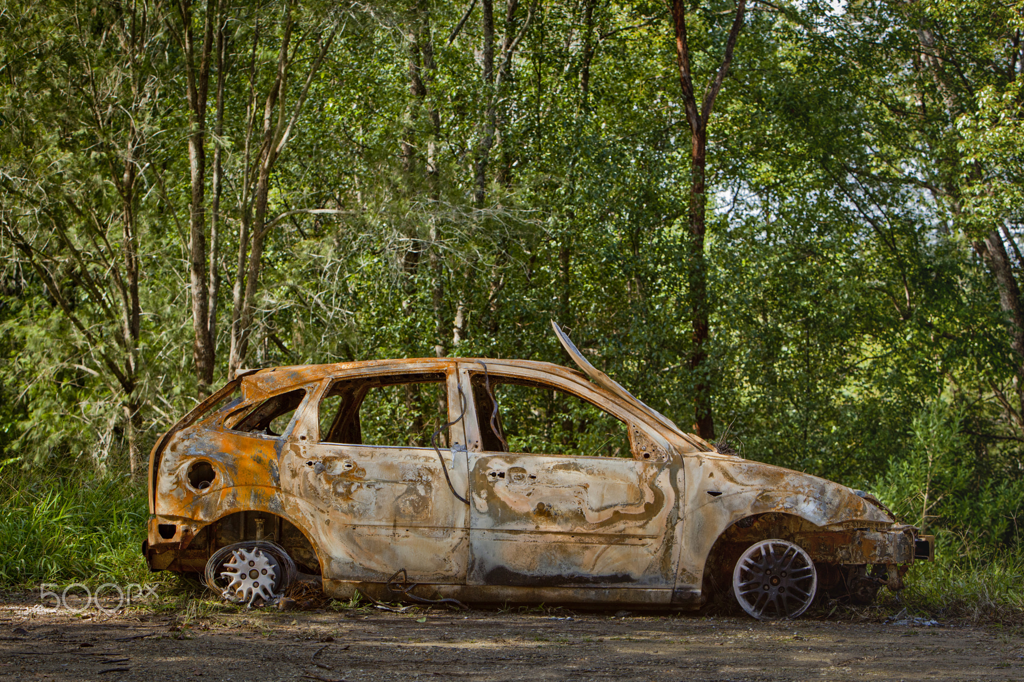 Burned and abandoned vehicle stationary in the forest, among the trees