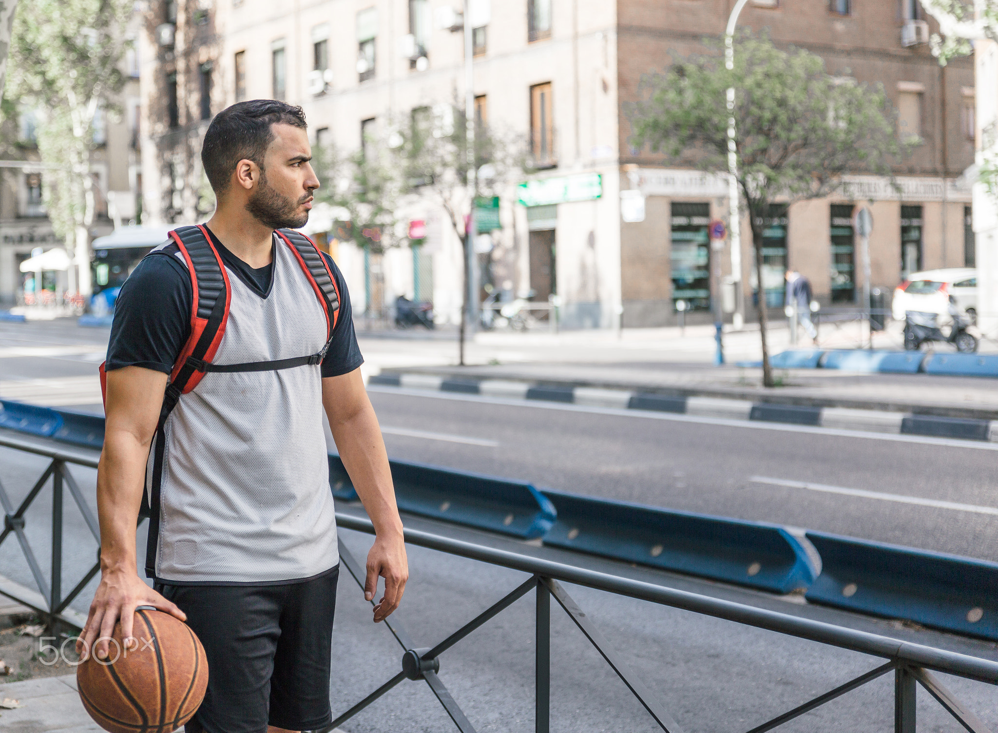 Basketball player walks down the street with a red backpack and his basket ball