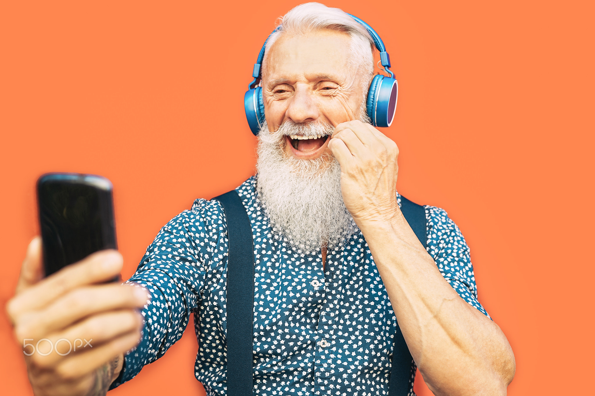 Senior bearded man taking selfie with mobile phone while listening favorite playlist with headphones