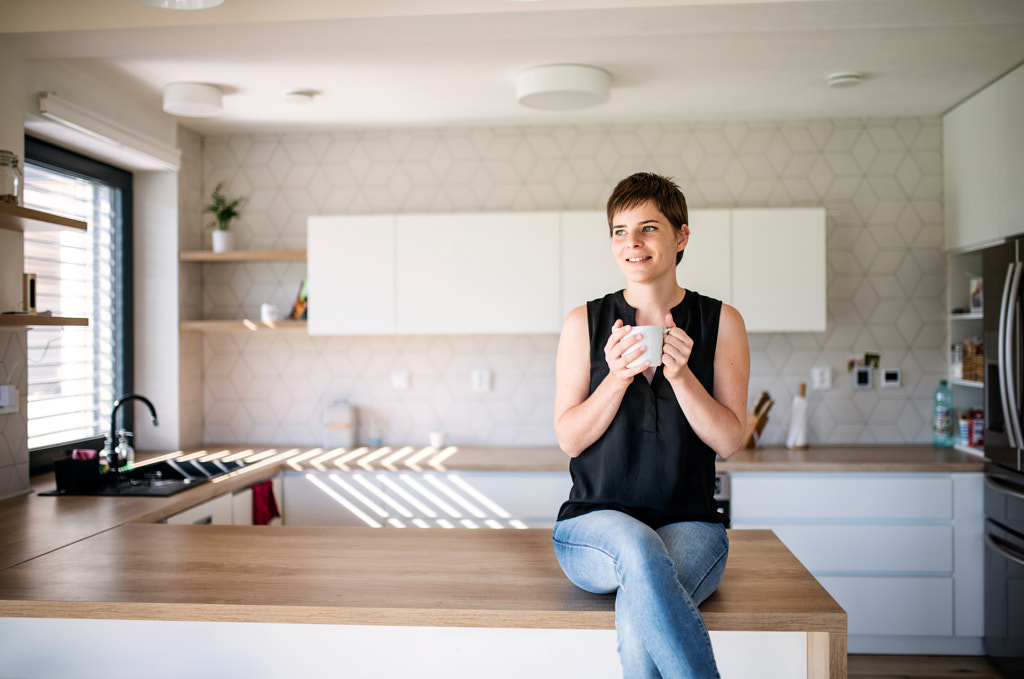 Front view of young woman with coffee sitting indoors at home. by Jozef Polc on 500px.com