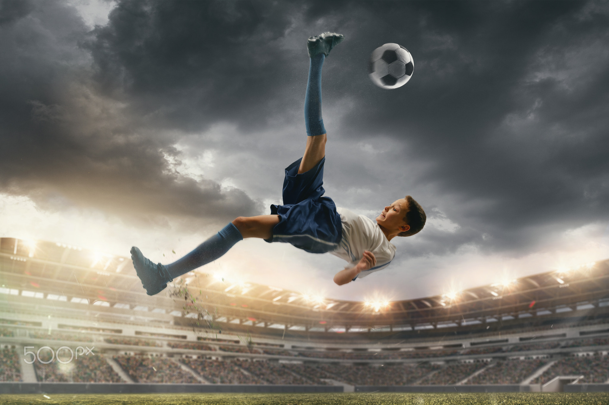 Young male soccer player kicking ball on stadium with flashlights on