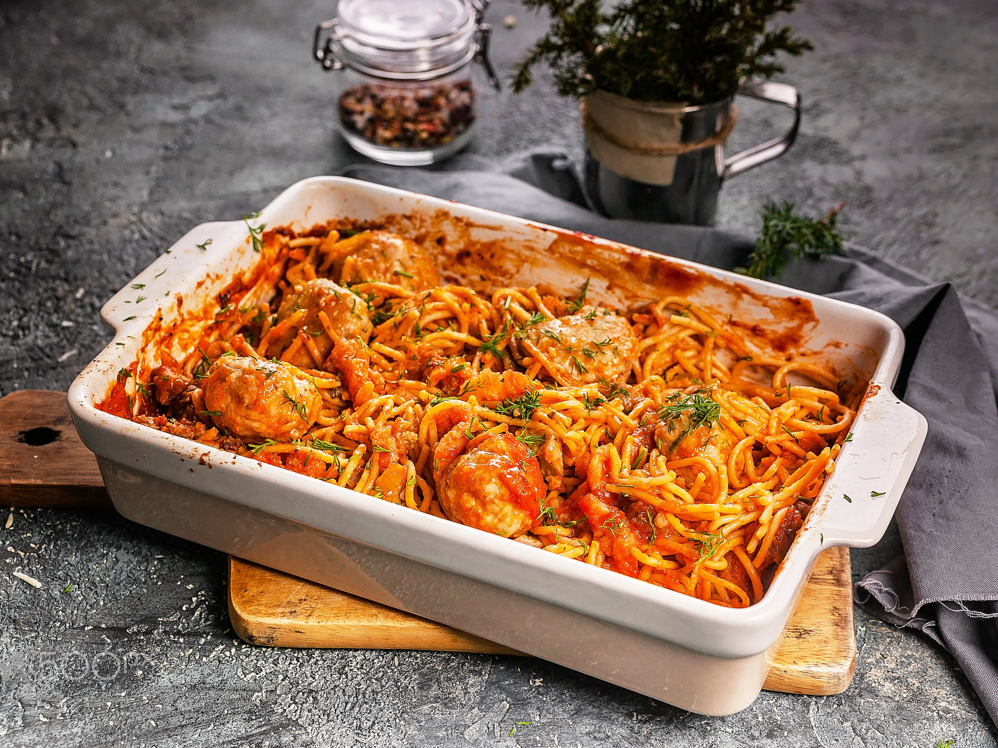 Spaghetti with meatballs with tomato sauce and herbs in a baking dish.