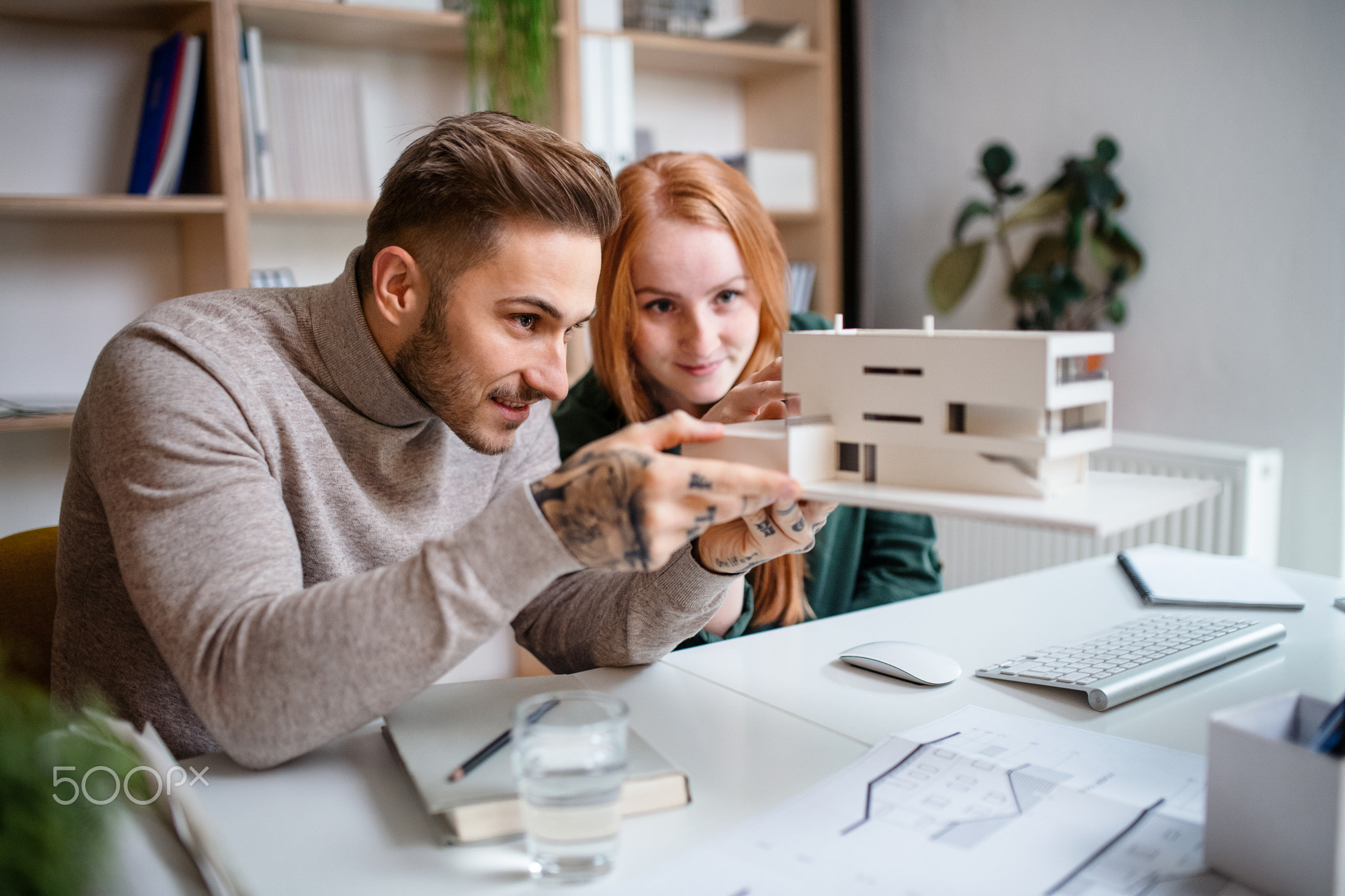 Architects with model of house sitting at the desk indoors in office