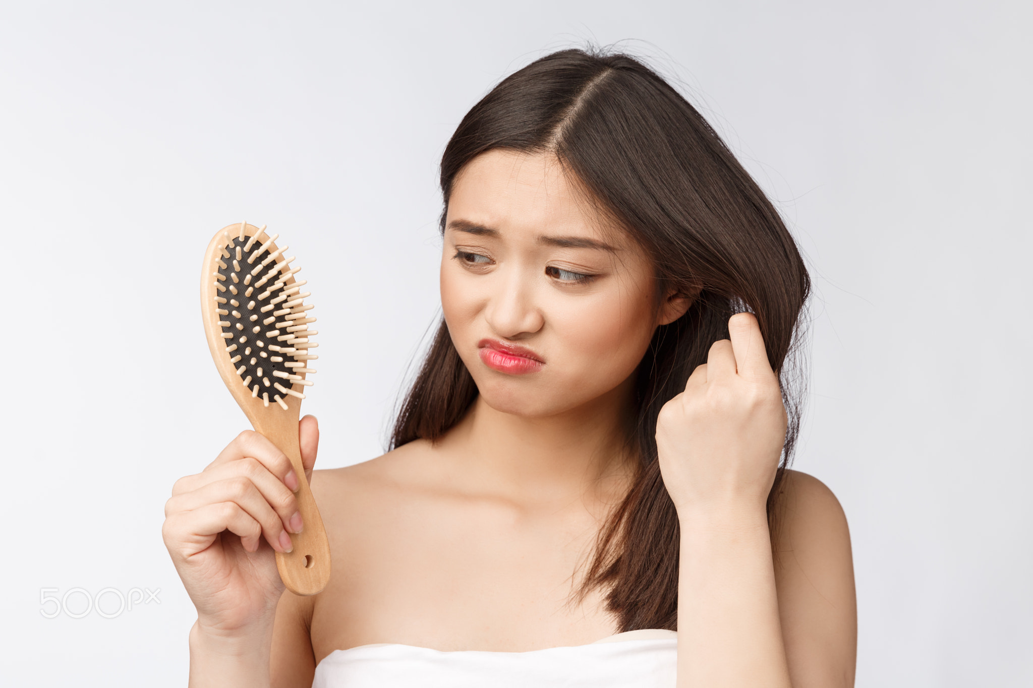 Upset stressed young Asian woman holding damaged dry hair on hands