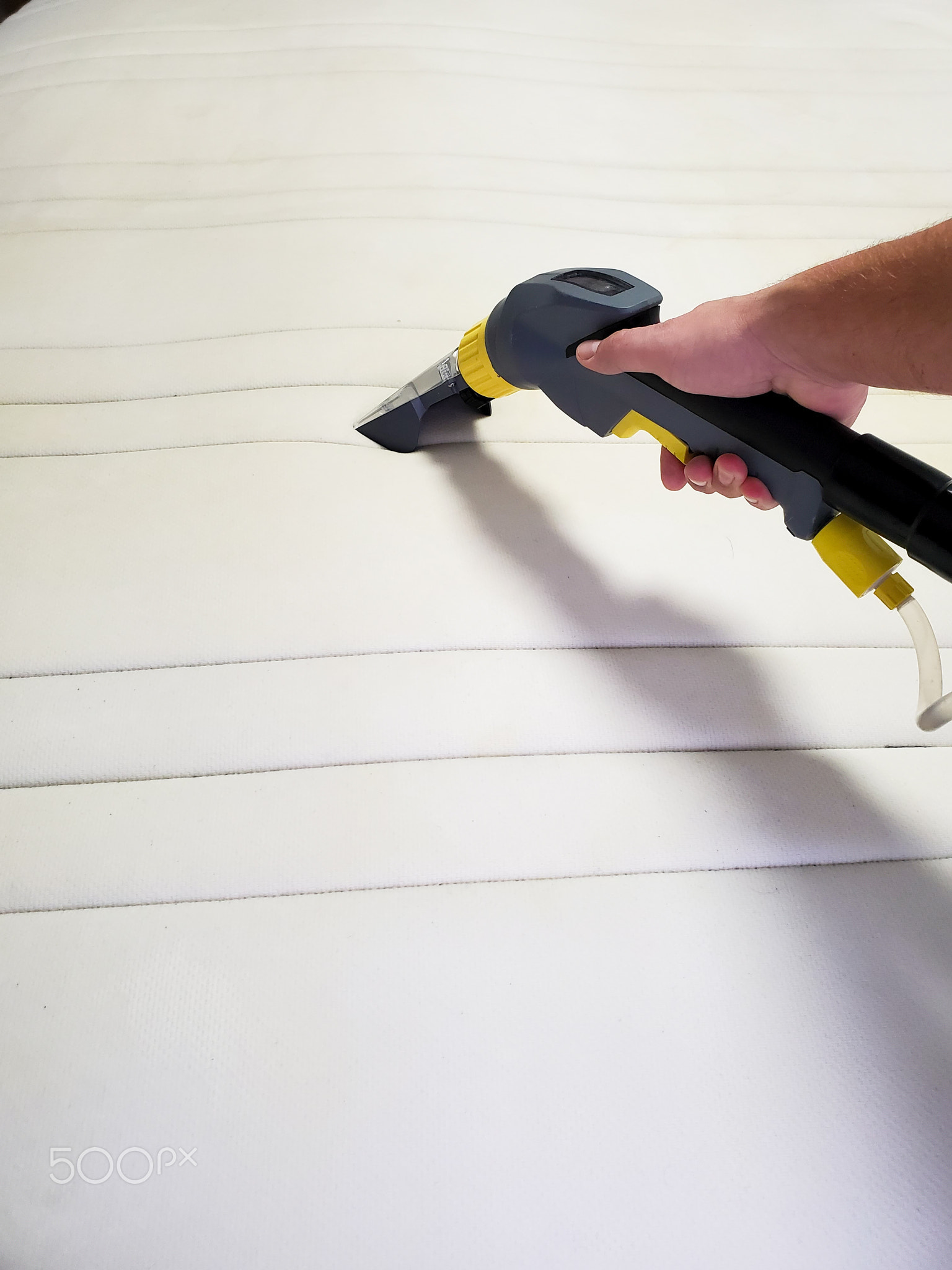 man's hand cleans a modern white mattress with a professional cleaning