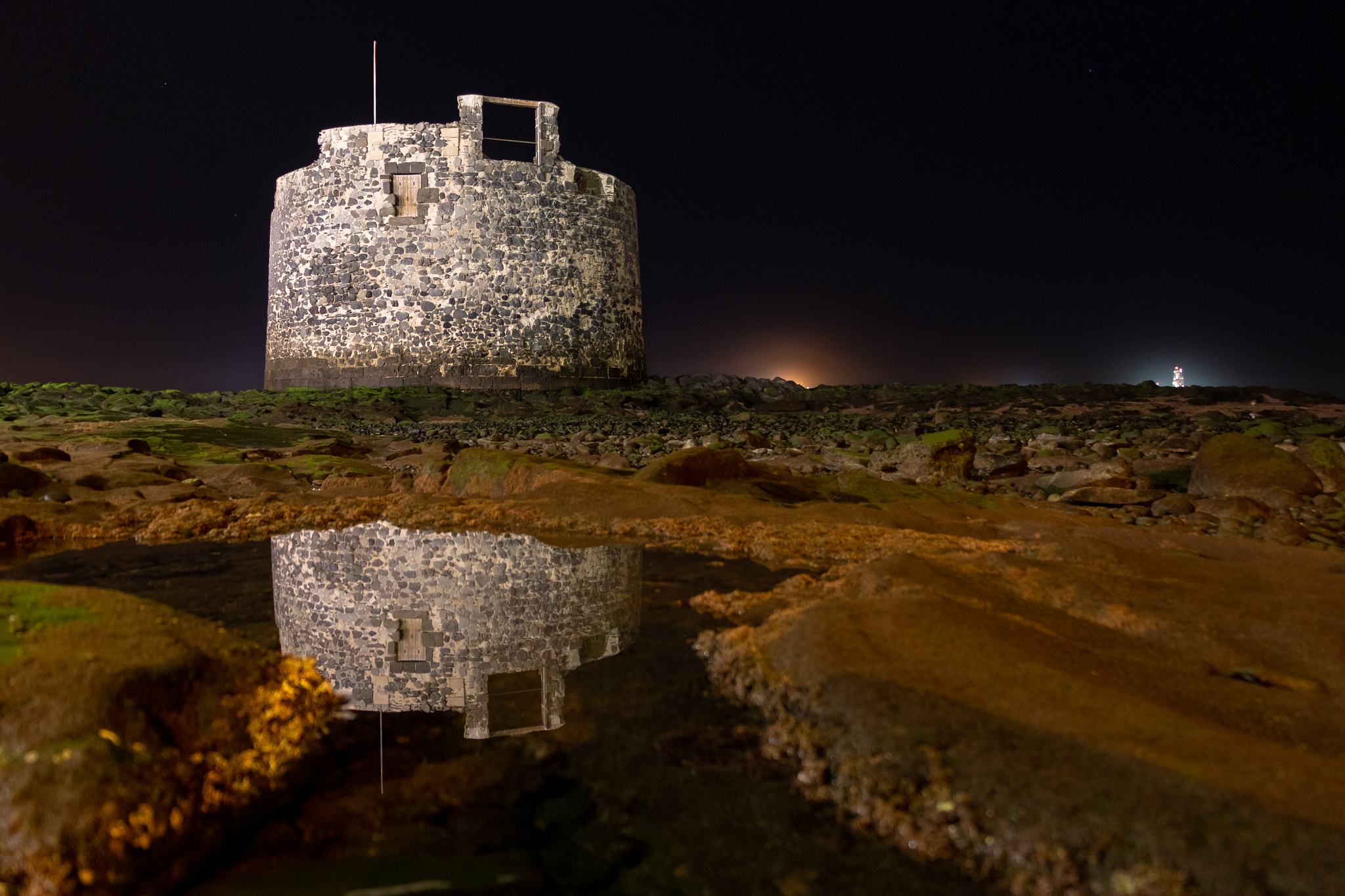 Medieval defensive tower next to the beach at night and its reflection