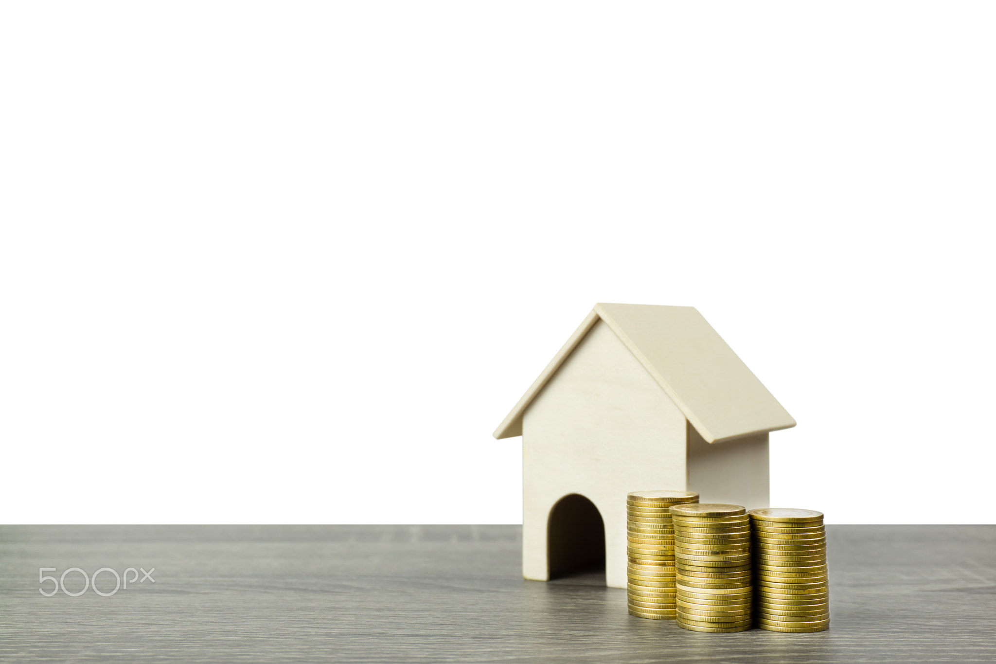 A small wooden house model with stack of golden coins on wood table.