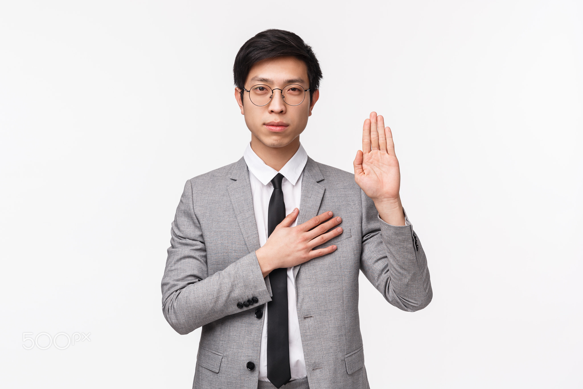 Waist-up portrait of devoted good-looking asian young man in grey suit