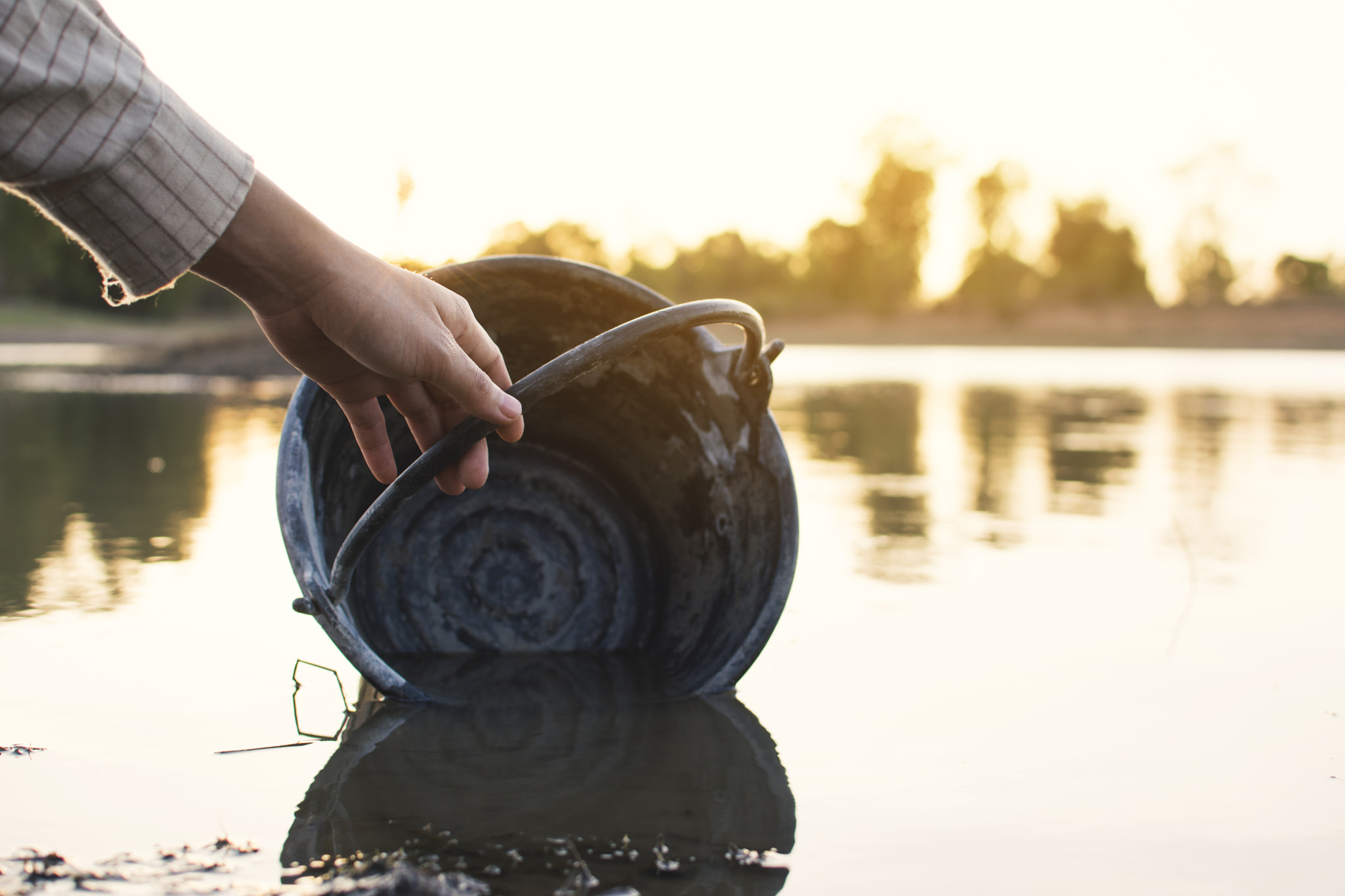 hand of woman holding a bucket on lake, crisis of water and drought