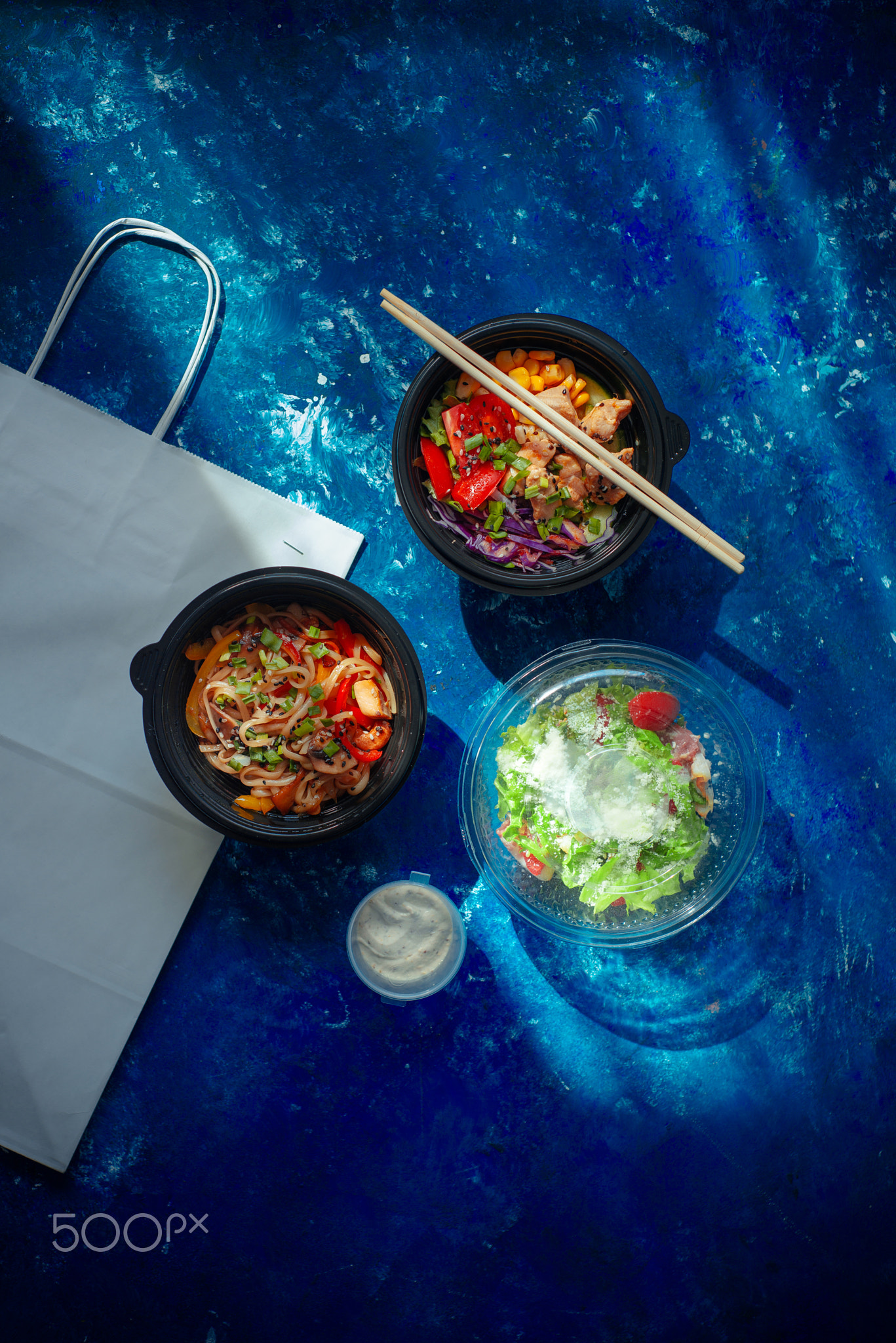 Take out flat lay with poke with chicken, udon and Ceasar salad in