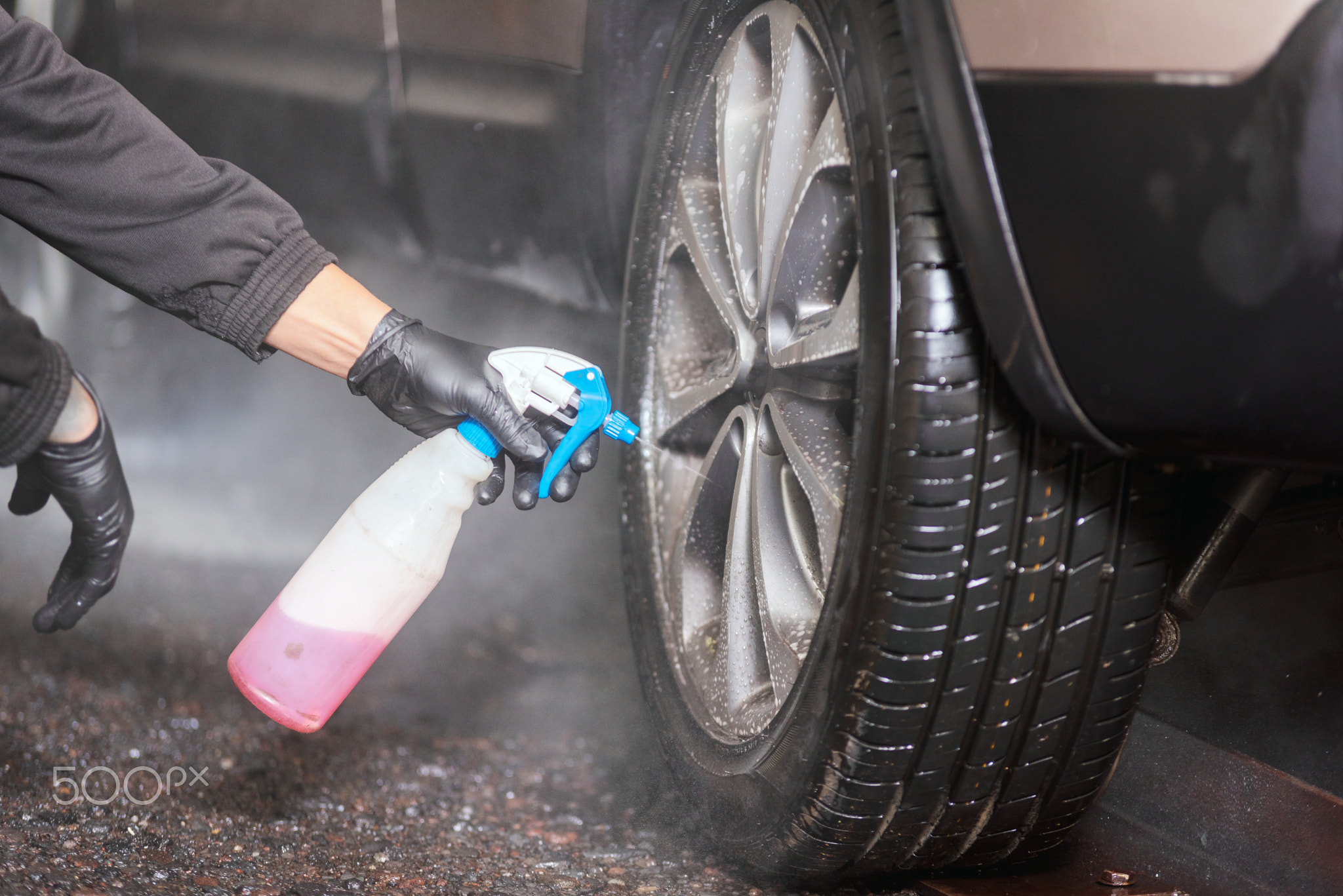 Professional car washer cleaning alloy wheels.