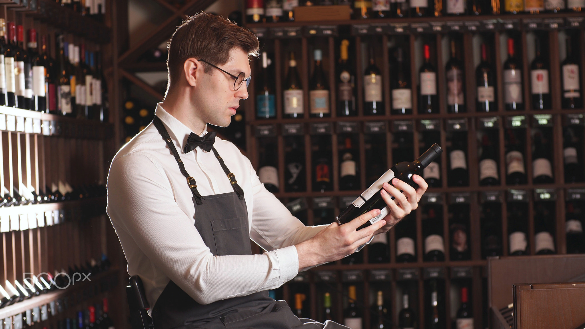 Elegant wine seller or cavist, offers a bottle of red wine, a man