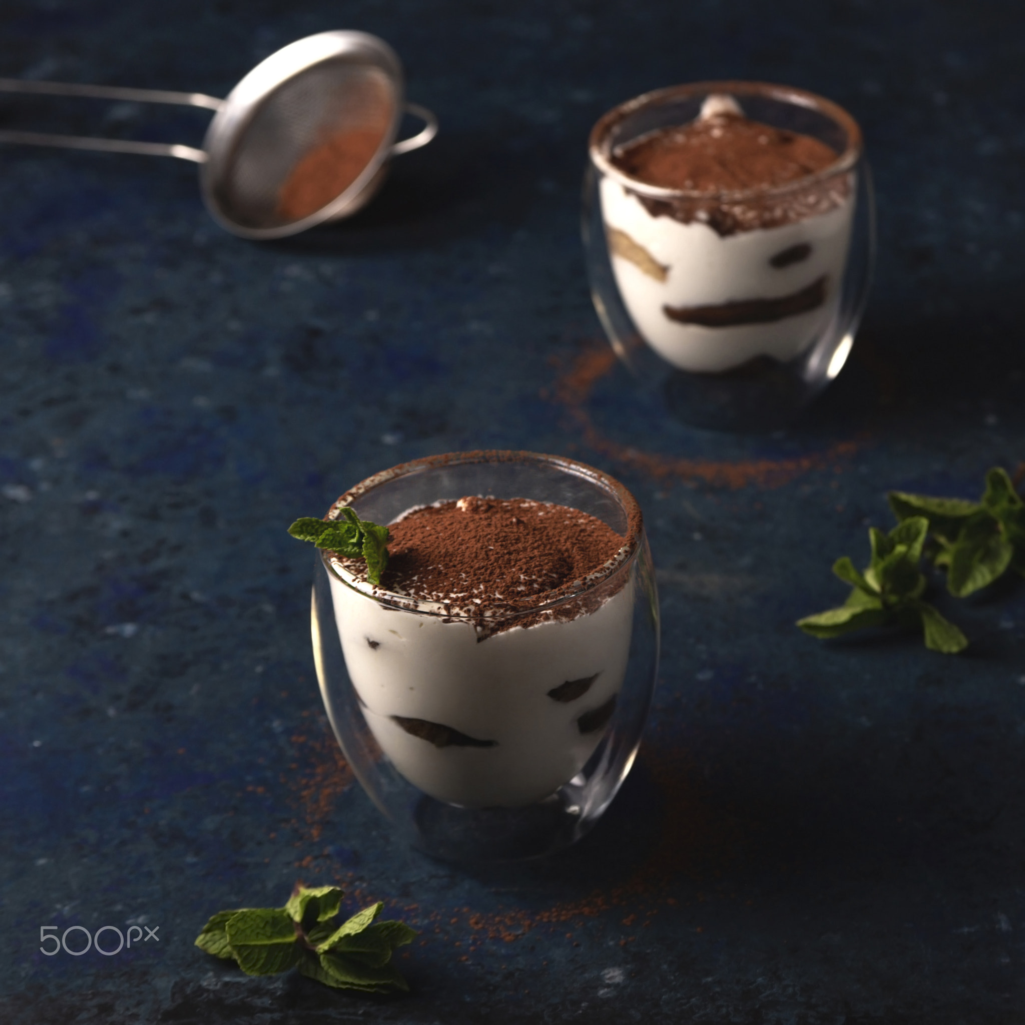 Two servings of tiramisu garnished with cocoa and mint