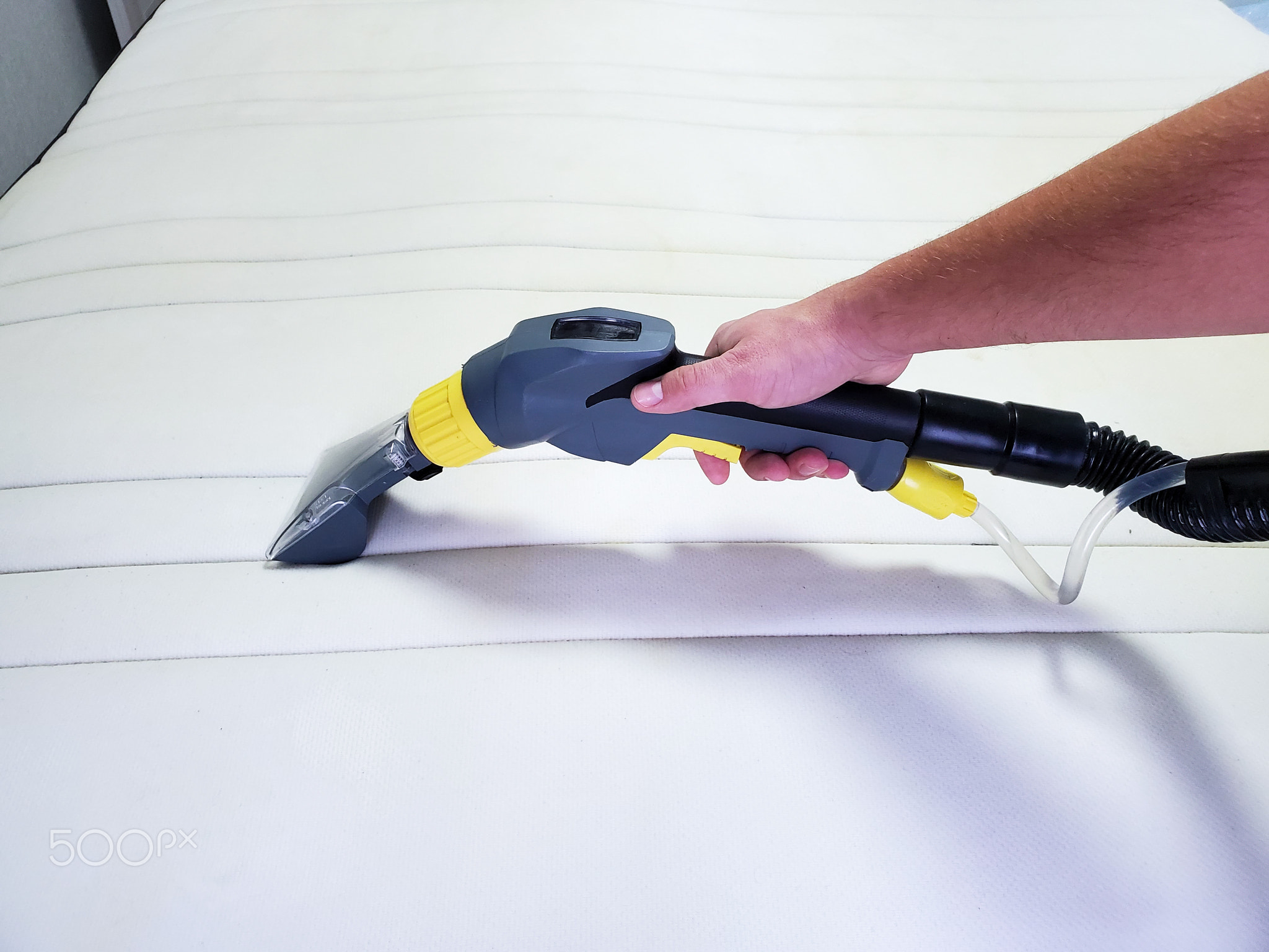 man's hand cleans a modern white mattress with a professional cleaning