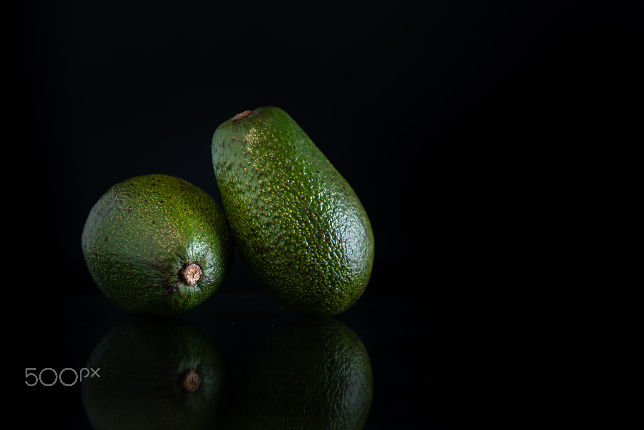 two whole avocados with reflection and copy space on a black