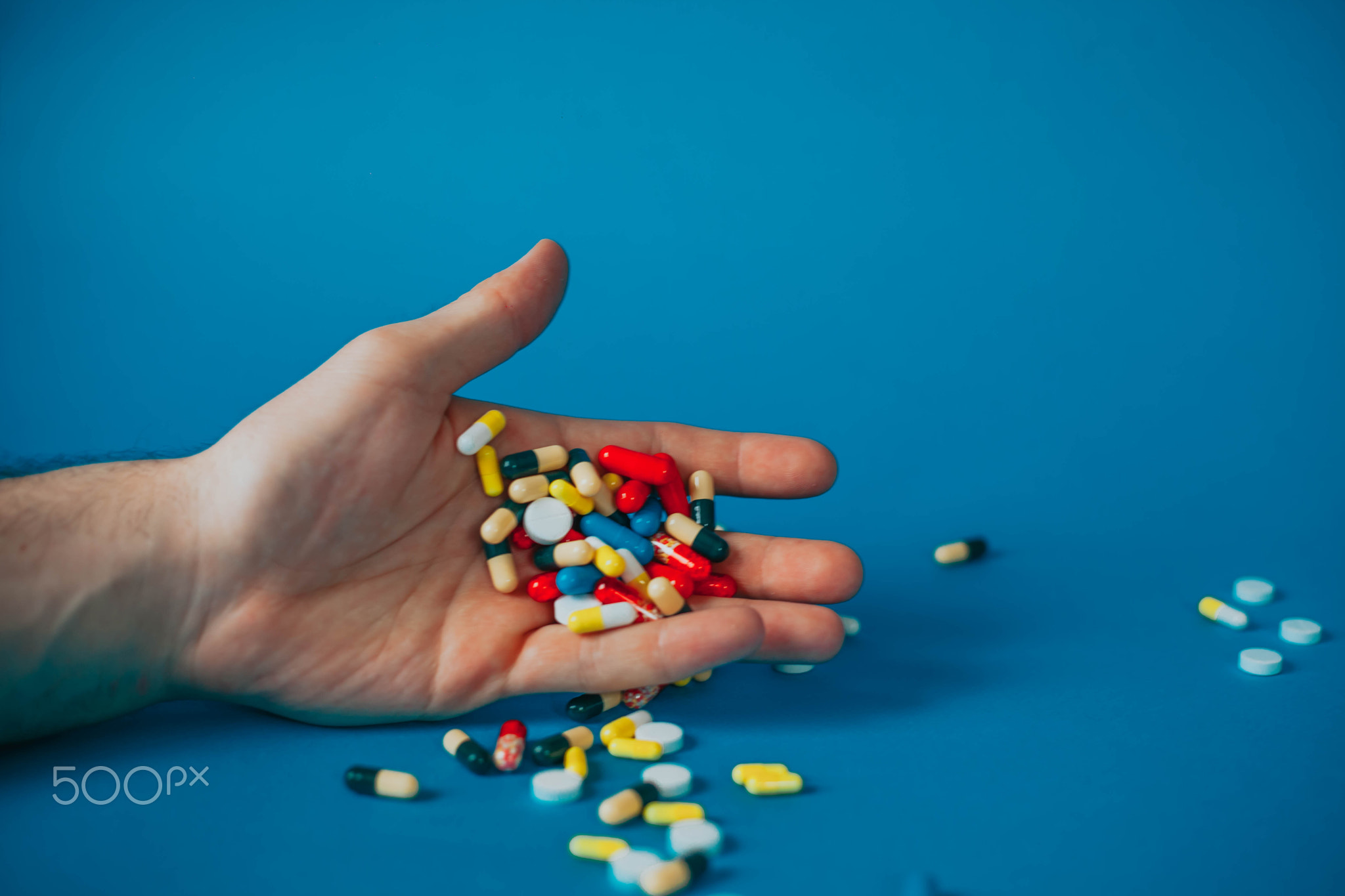 a bunch of different pills in a man's hand on a blue background