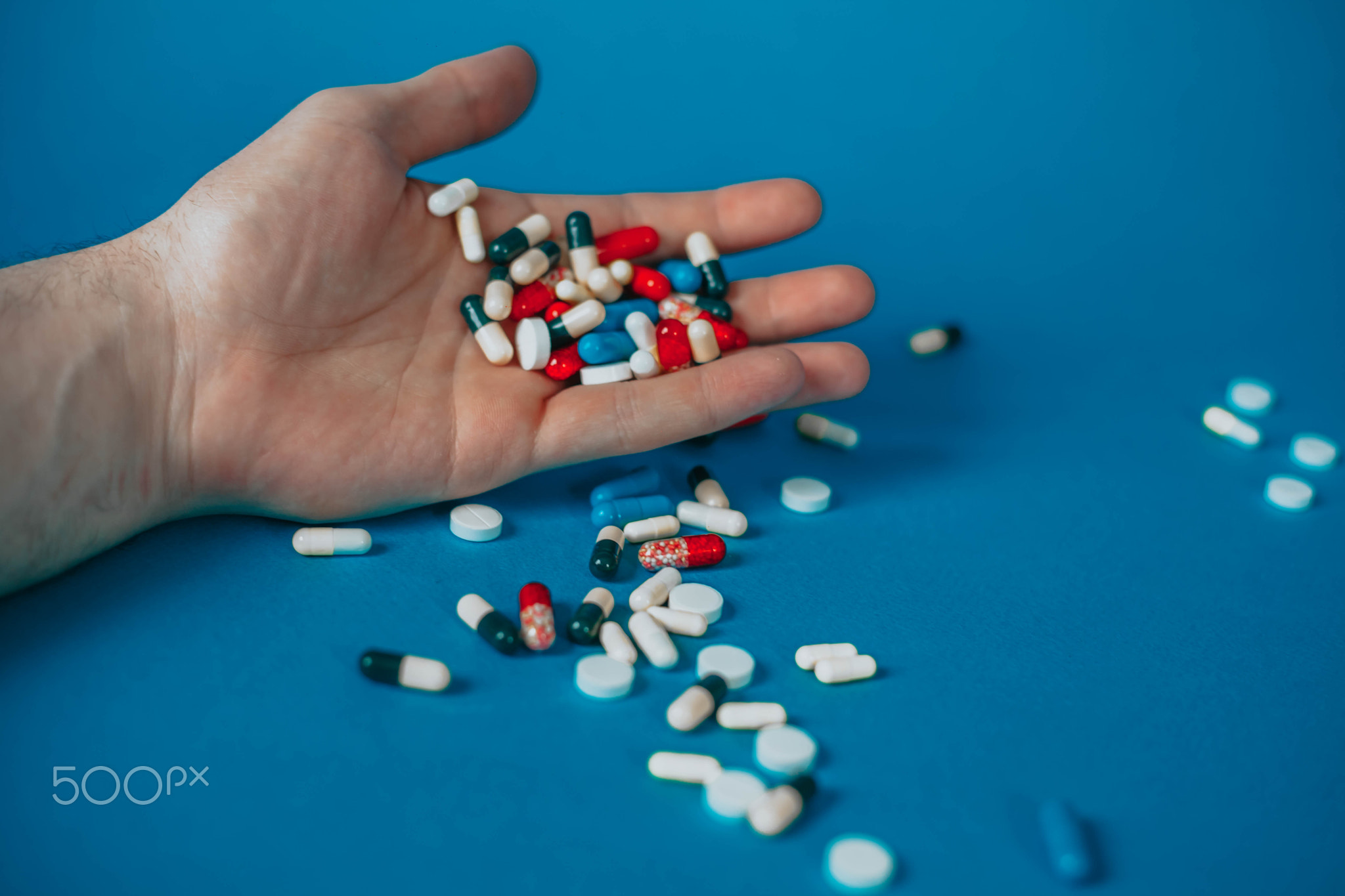 a bunch of different pills in a man's hand on a blue background