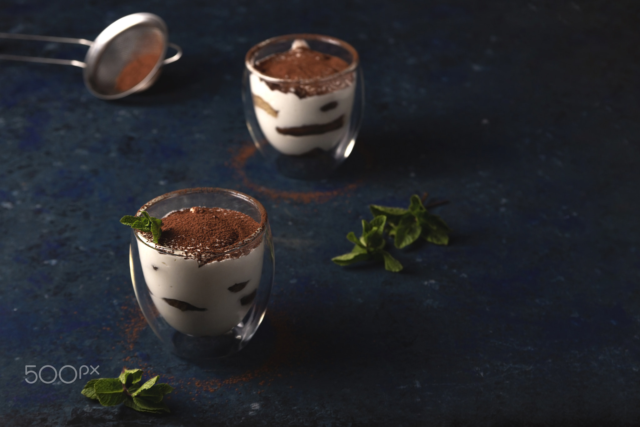 Two servings of tiramisu garnished with cocoa and mint