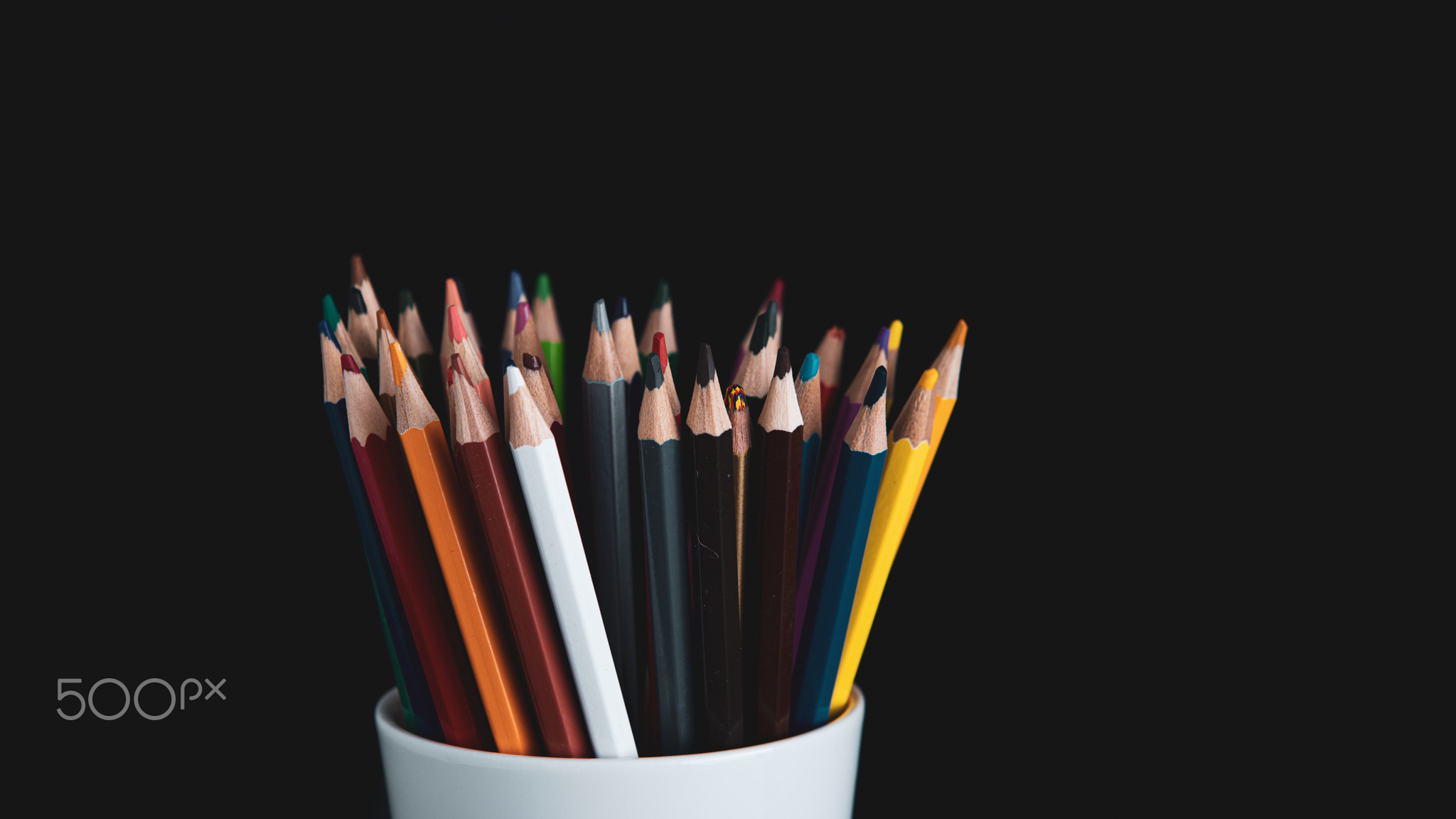 colored pencils in white cup on a black background