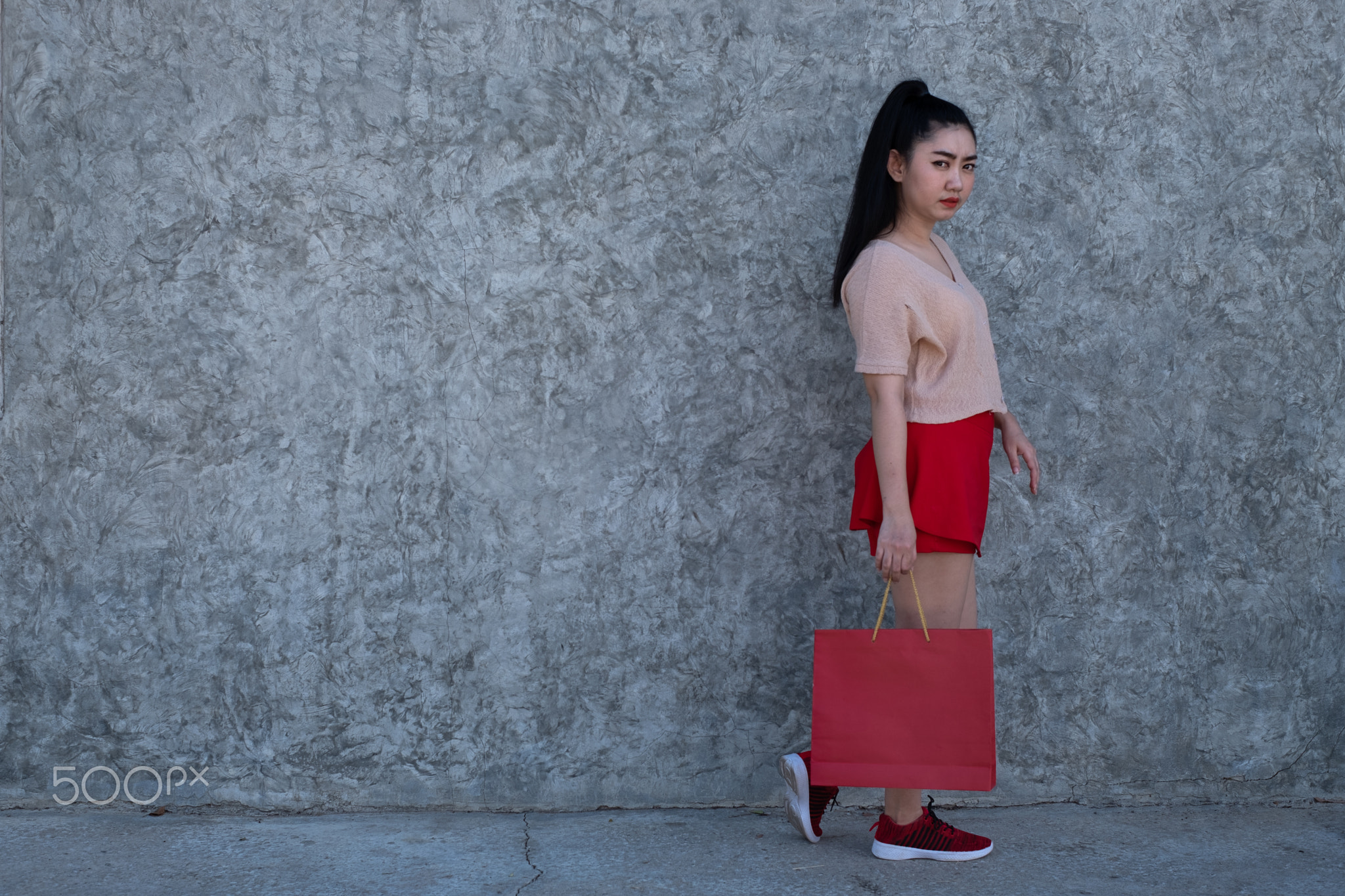 young Asia woman holding shopping bags at concrete wall background