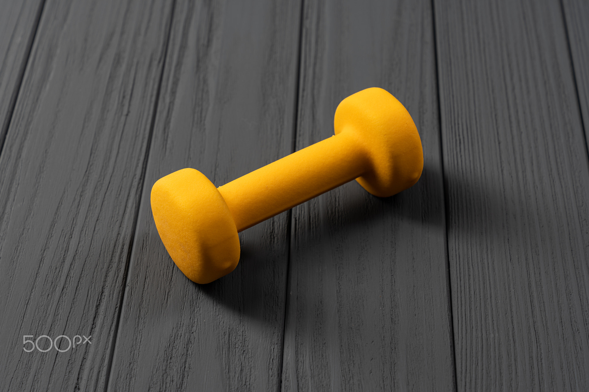 Single yellow dumbbell in the middle of an image isolated on wooden