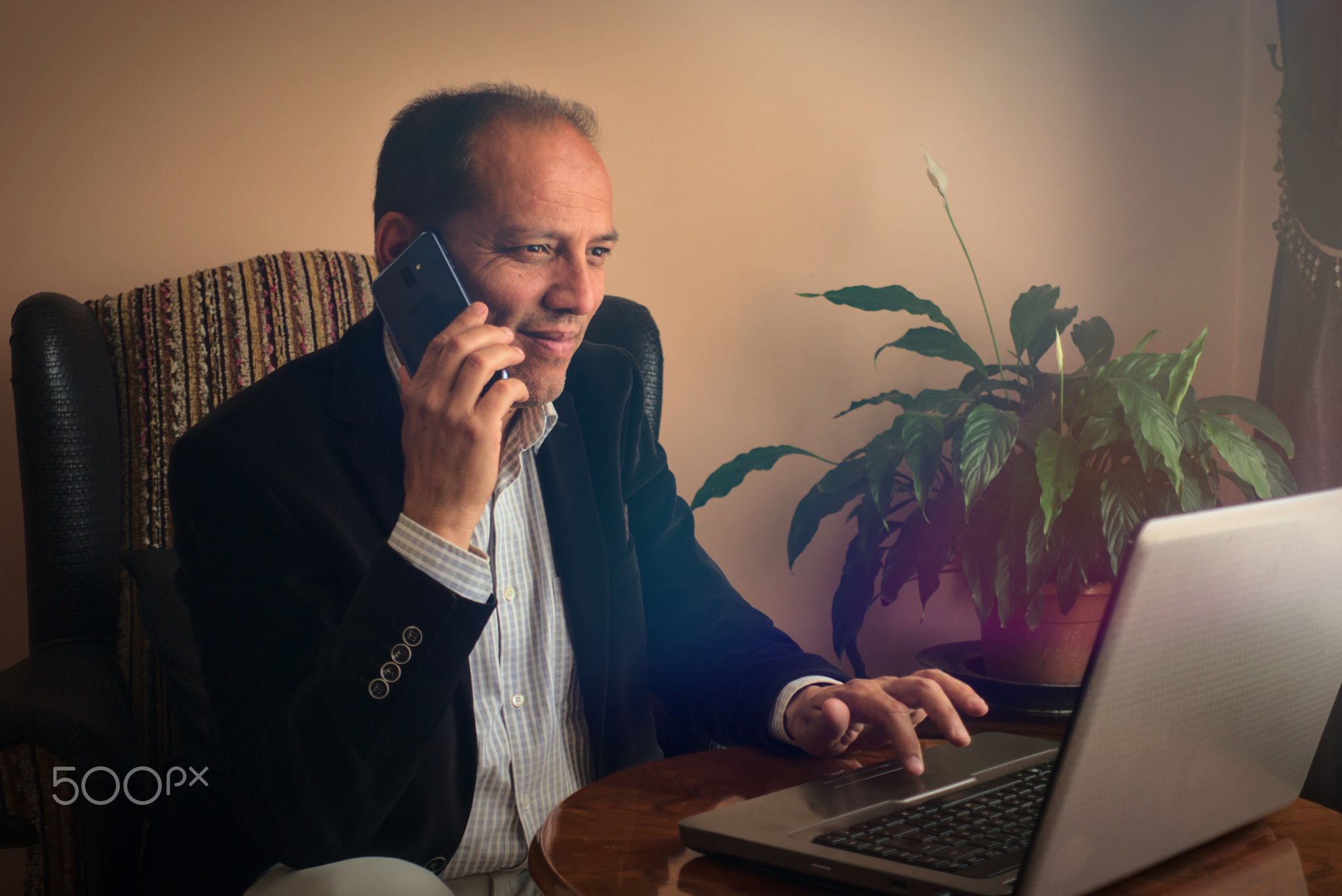 Smiling senior man sitting on armchair phoning to a friend at home