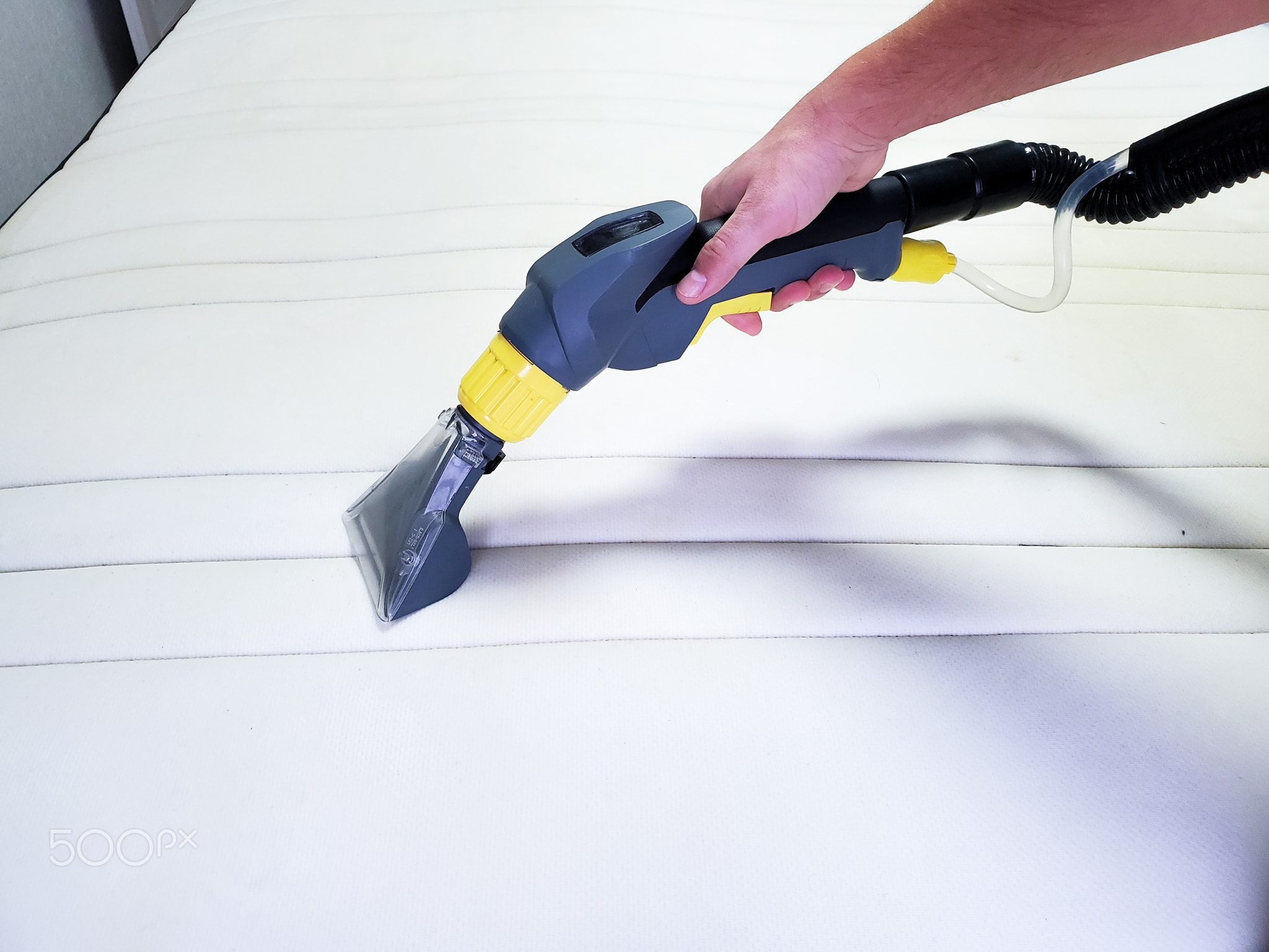 man's hand cleans a modern white mattress with a professional cleaning