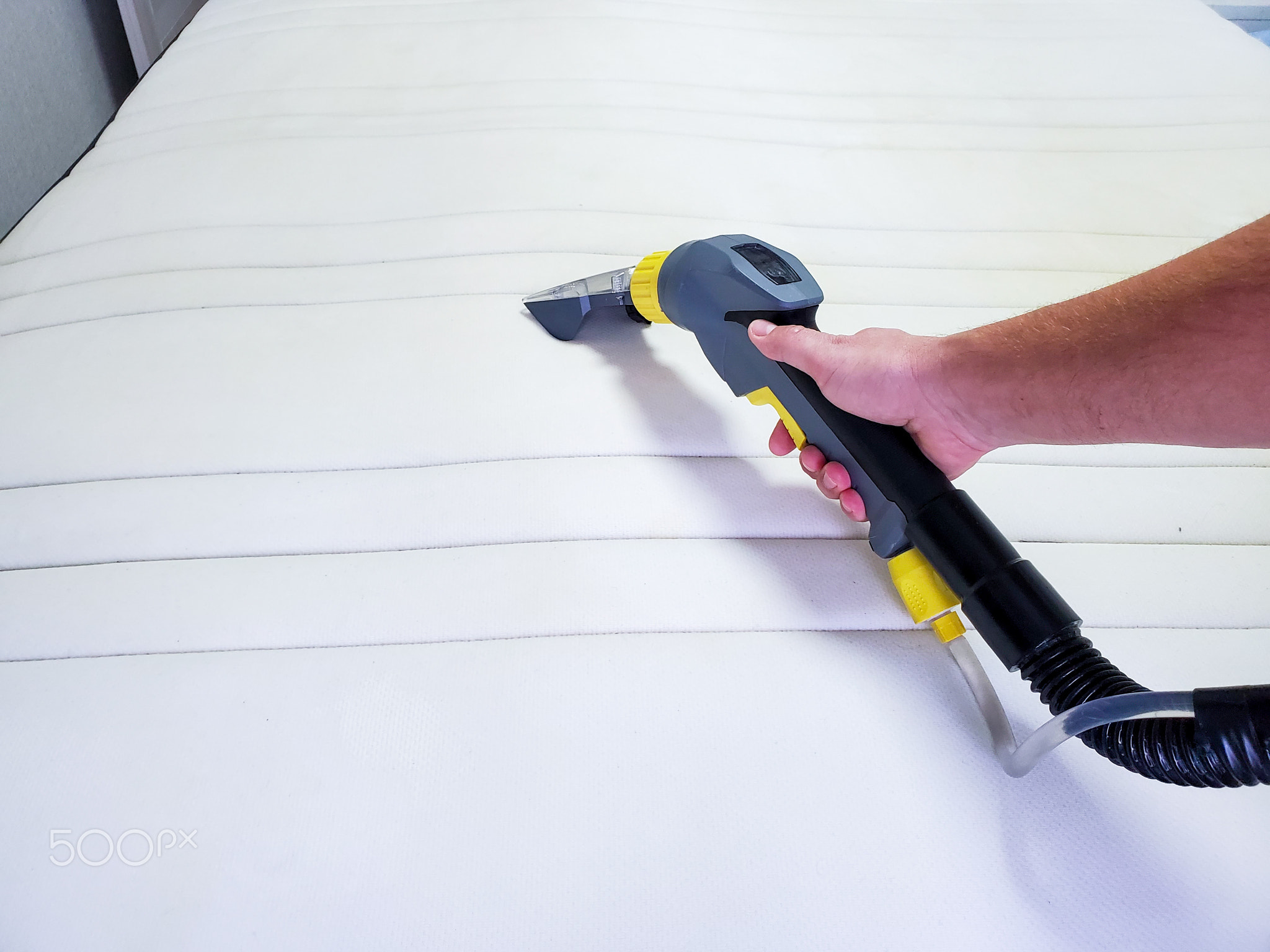 man's hand cleans a modern white mattress with a professional cleaning