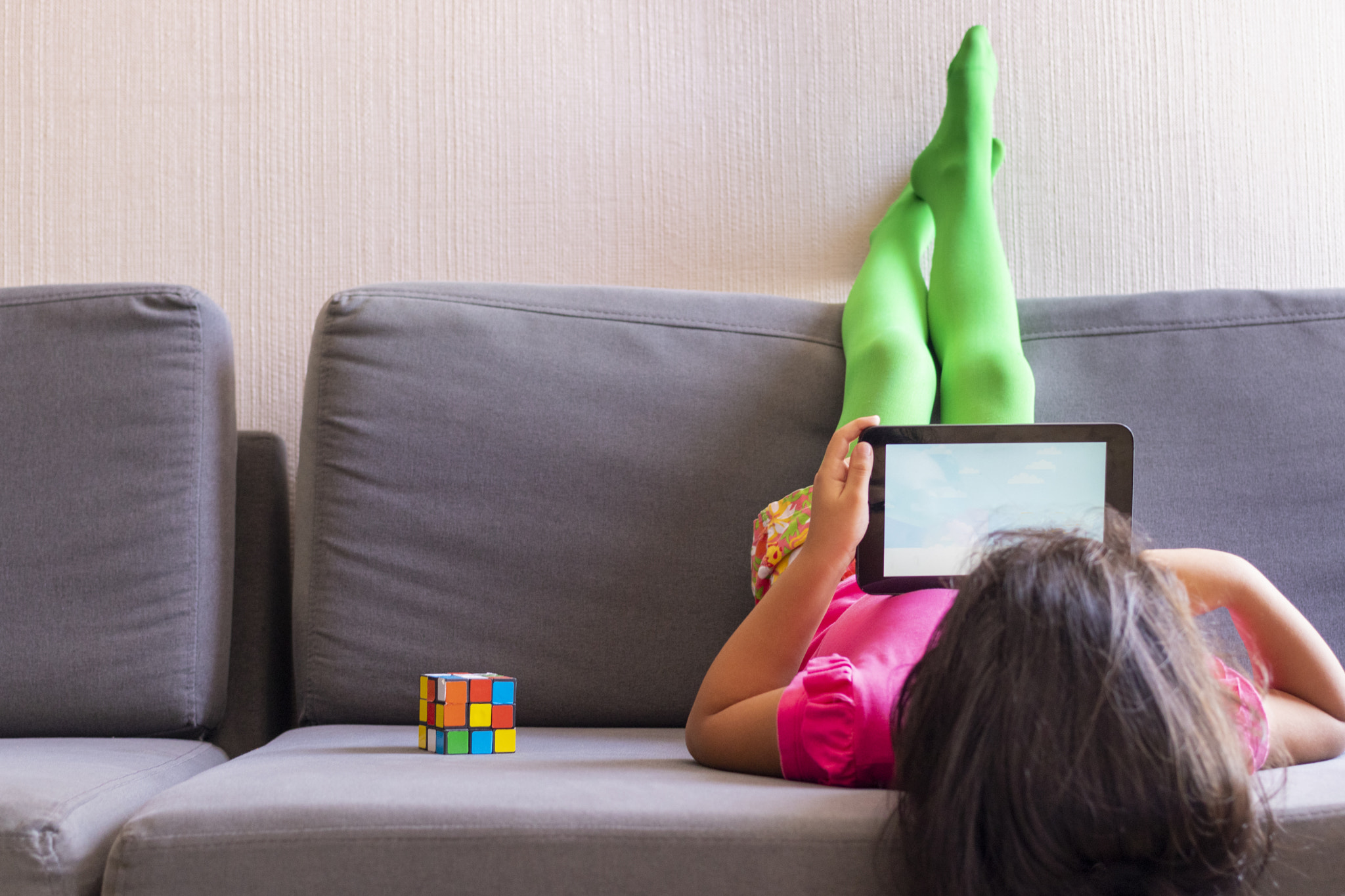 Little girl playing with her tablet lying on the sofa